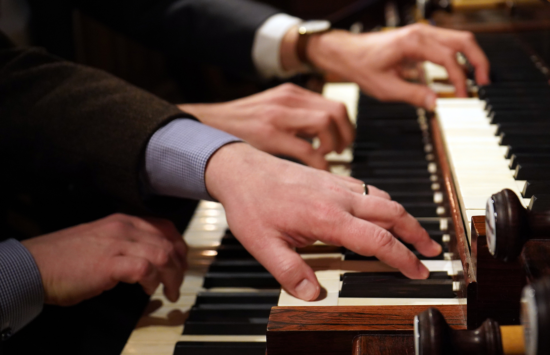 Två par händer spelar tillsammans på Åkermanorgelns klaviatur. I förgrunden syns spakarna för de utdragna valda registren.