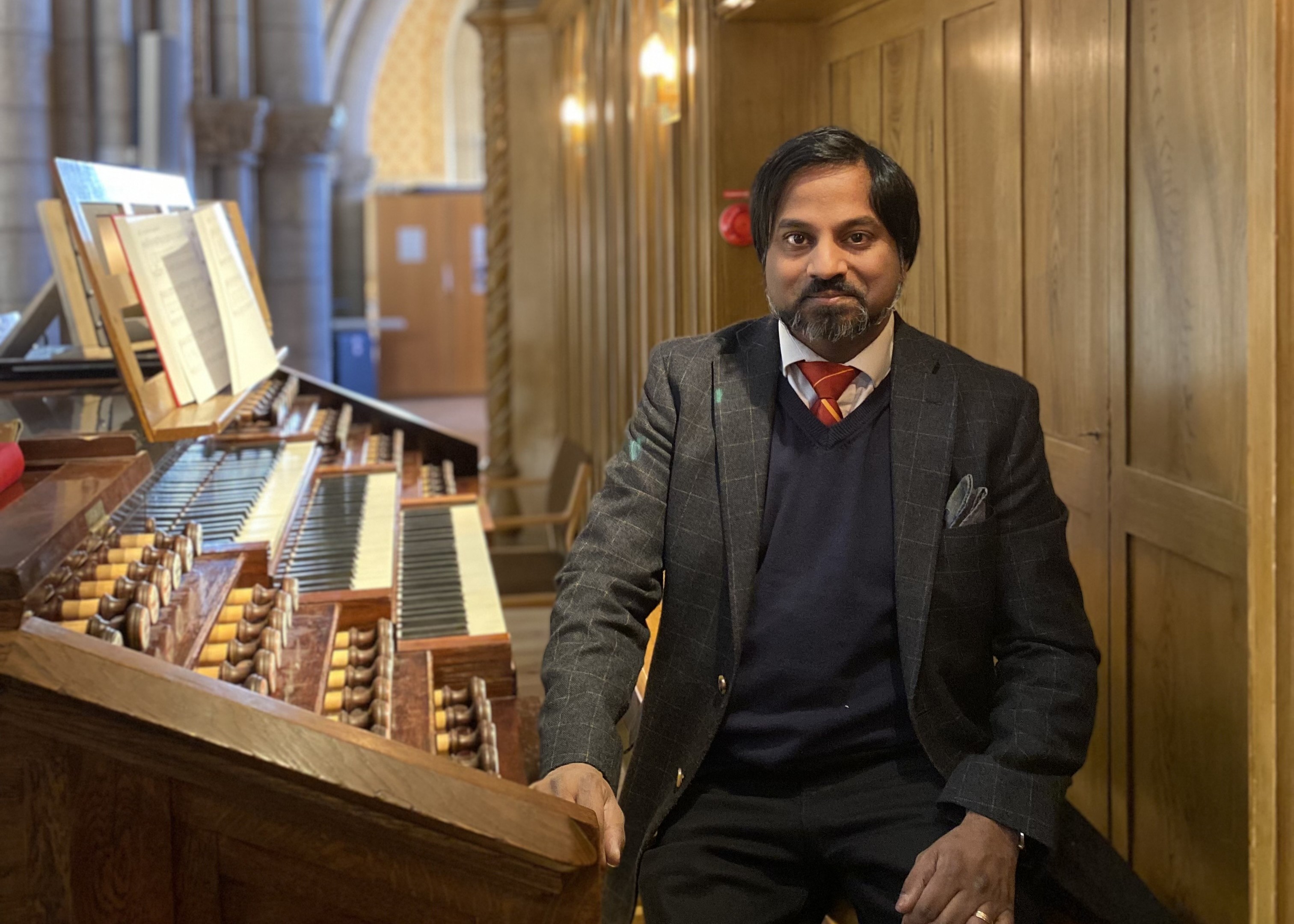 Johnny Larsson i rutig kavaj, röd slips och blå slipover på orgelpallen vid Åkermanorgelns spelbord uppe på Västra läktaren i Uppsala domkyrka.