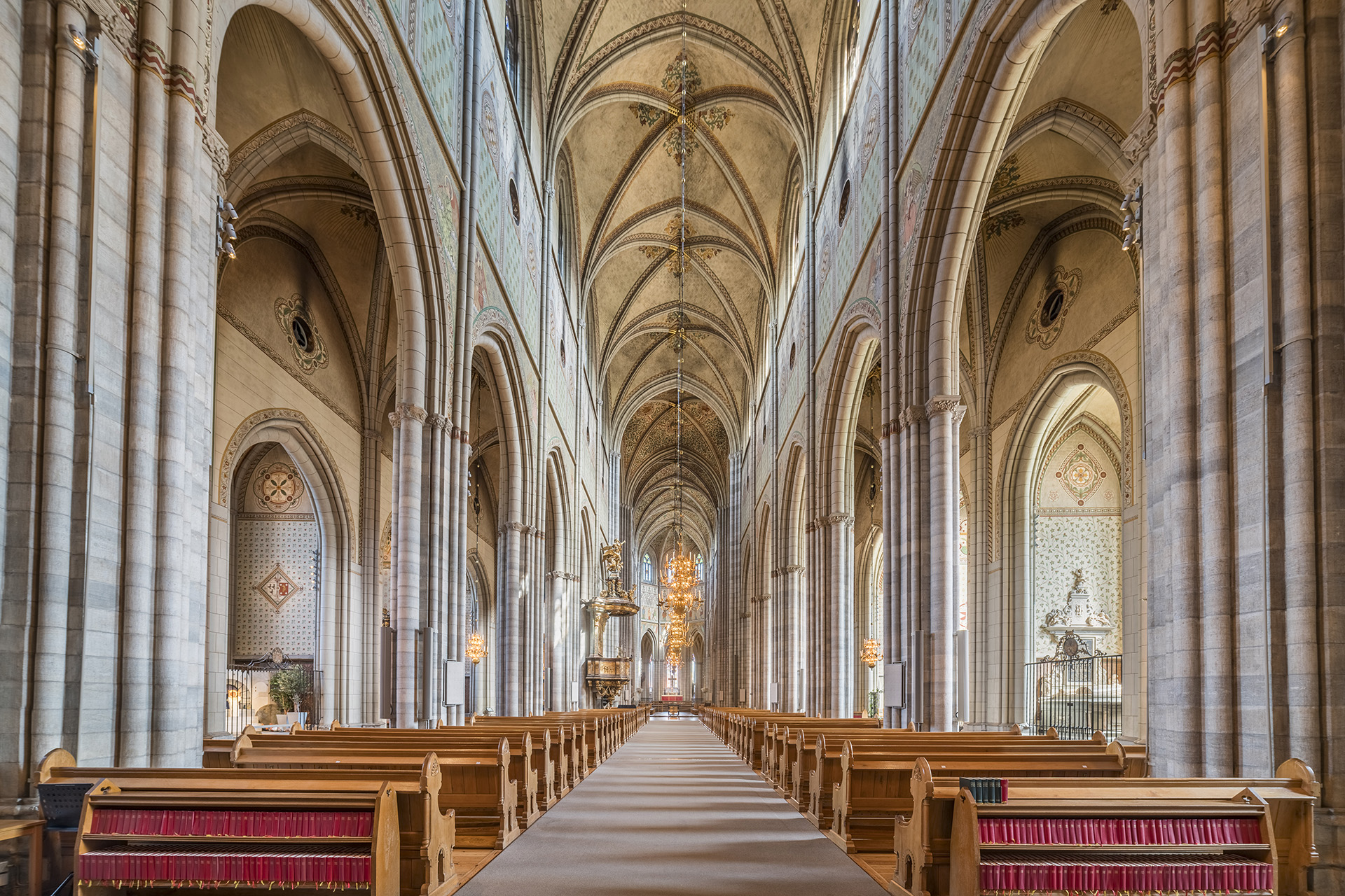 Storslagen vy över sommarupplsta Uppsala domkyrkas kyrkorum, med mittskeppets pelargång som sträcker sig hela vägen fram till högaltaret.