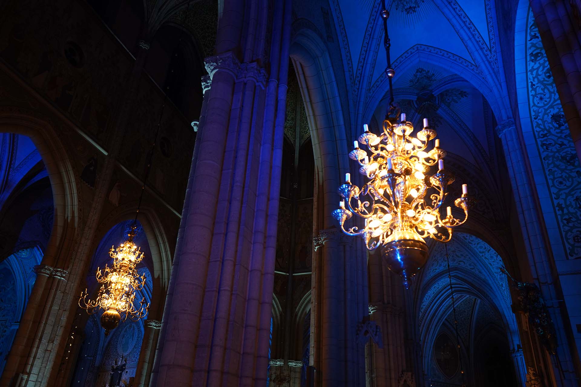 Uppsala domkyrkas ljuskronor avtecknar sig med strålande sken mot dramatiskt upplysta valv i mörkblått och lila i samband med en konsert.