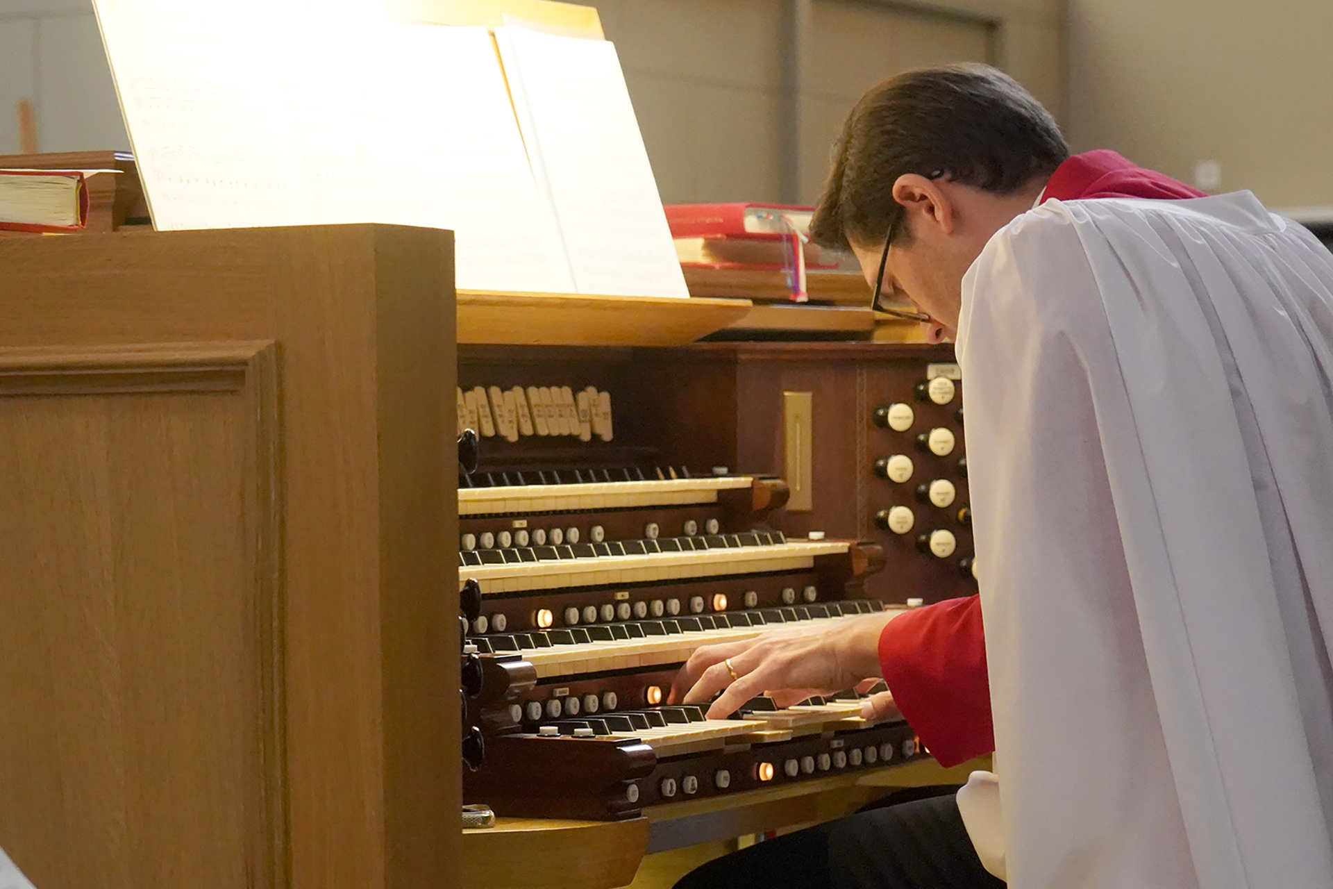 Organisten Robert bennesh ses hukad över Ruffattiorgelns spelbord, intensivt musicerande och iförd sin körledarkåpa i vitt och rött.