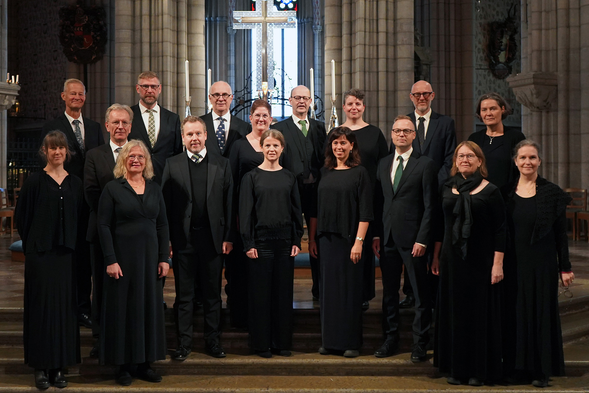 Uppsala katedralsångare, klädda i svart, uppställda i kortrappan i Uppsala domkyrka med högaltaret i bakgrunden.