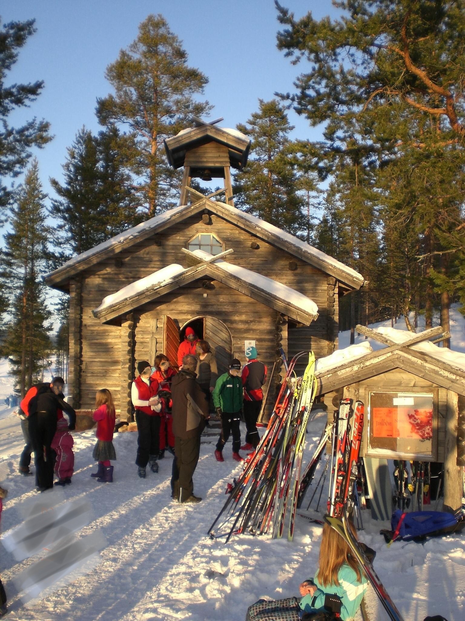 Träkapell i fjällmiljö med människor i skidkläder och skidor utanför.