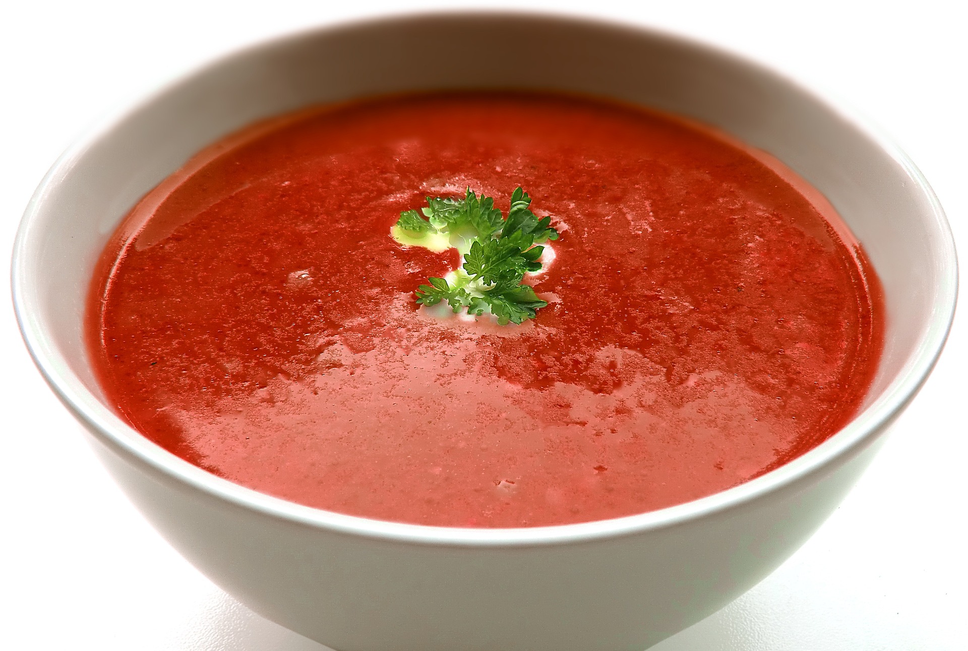 En djup tallrik med tomatsoppa och en persiljekvist.