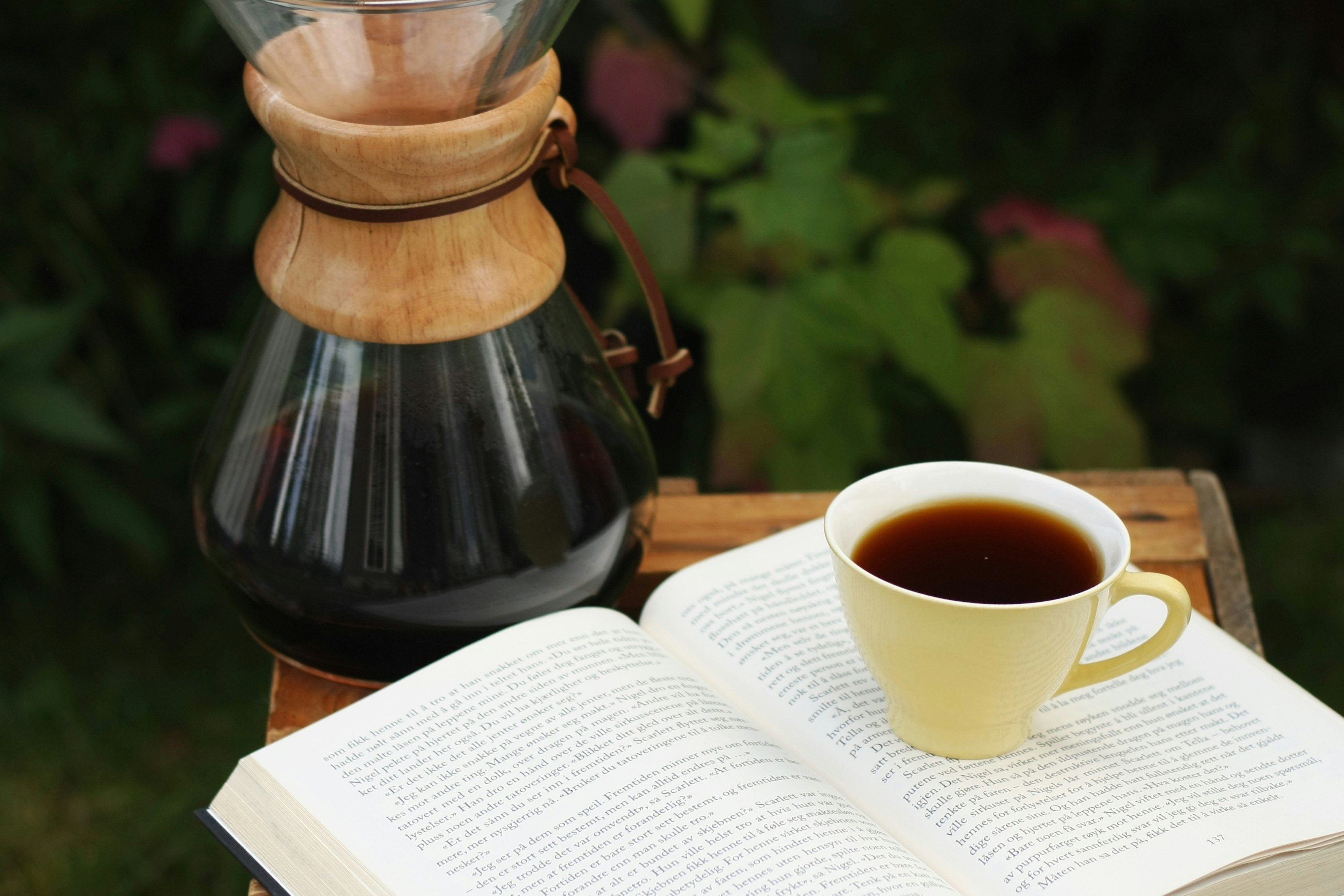 En kaffekopp och en bok i somrig miljö.