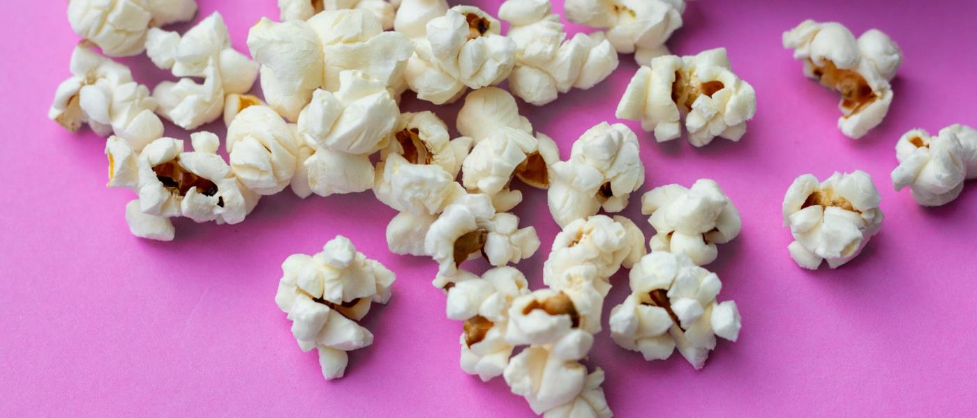 Poppade popcorn i skål hälls ut på lila bakgrund.