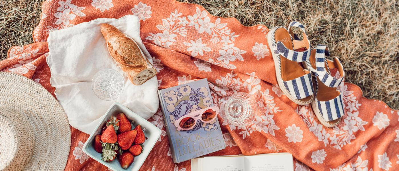 Bäcker på picknickfilt med jordgubbar, sandaler och solglasögon.