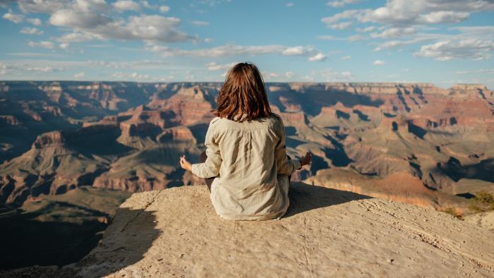 Kvinna sitter och mediterar med utsikt över ett bergsområde. 