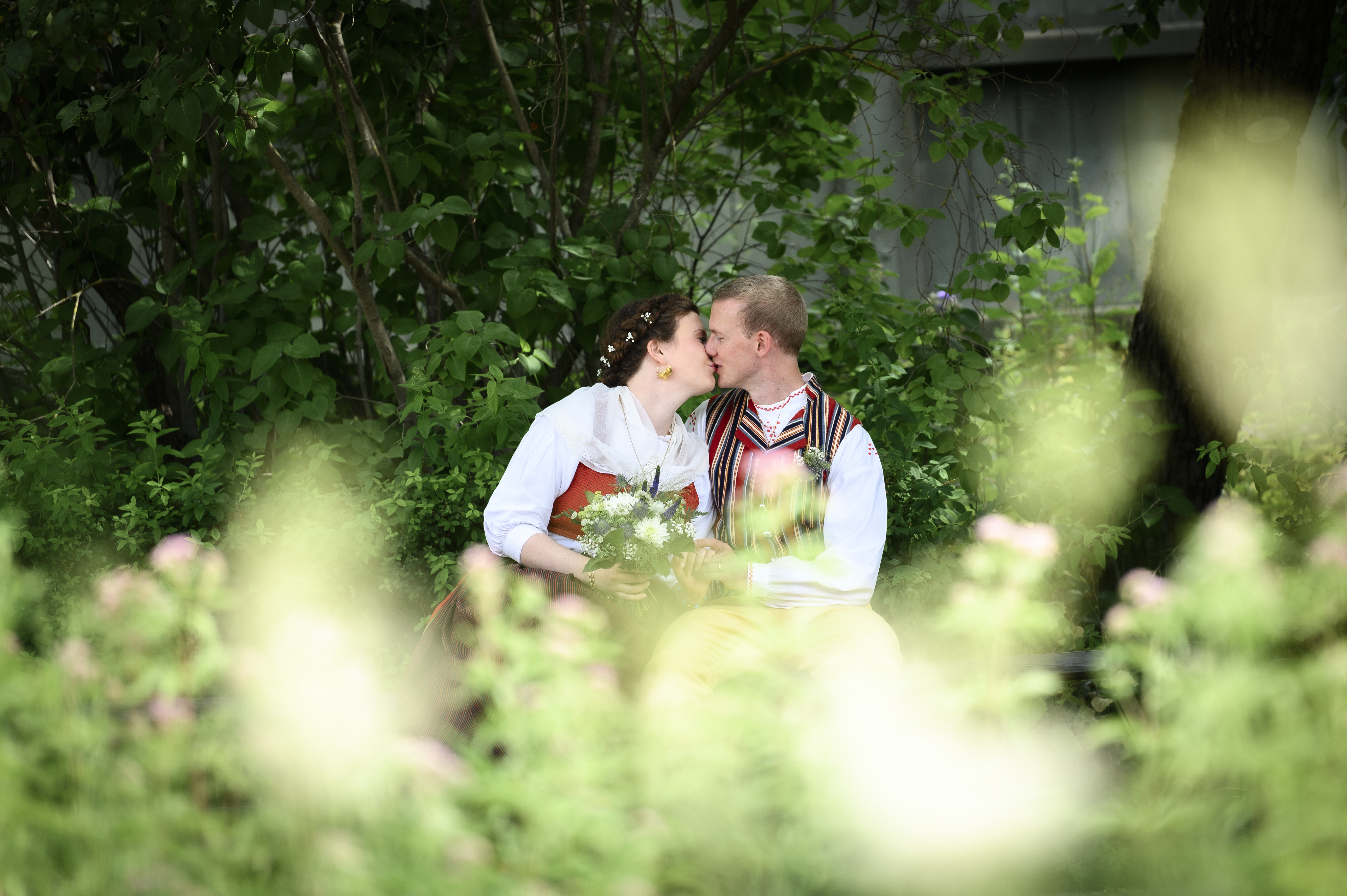 Ett nygift par kysser varandra i grönskande omgivningar. 