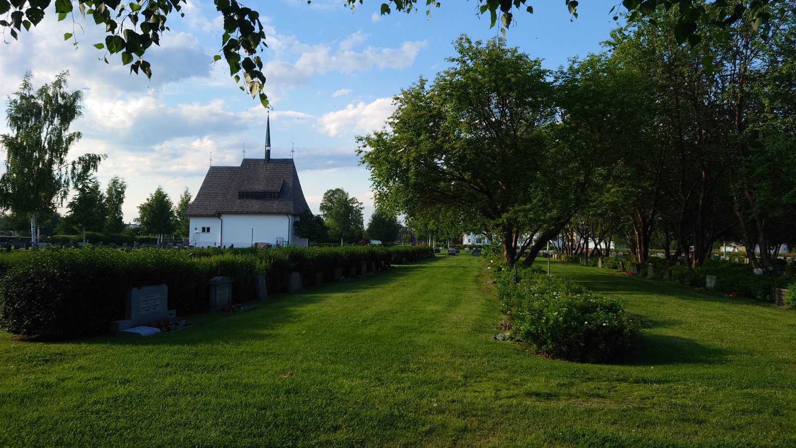 Bureå kyrkogård med gönskande gräsmatta, buskar och gravkapellet i bakgrunden.