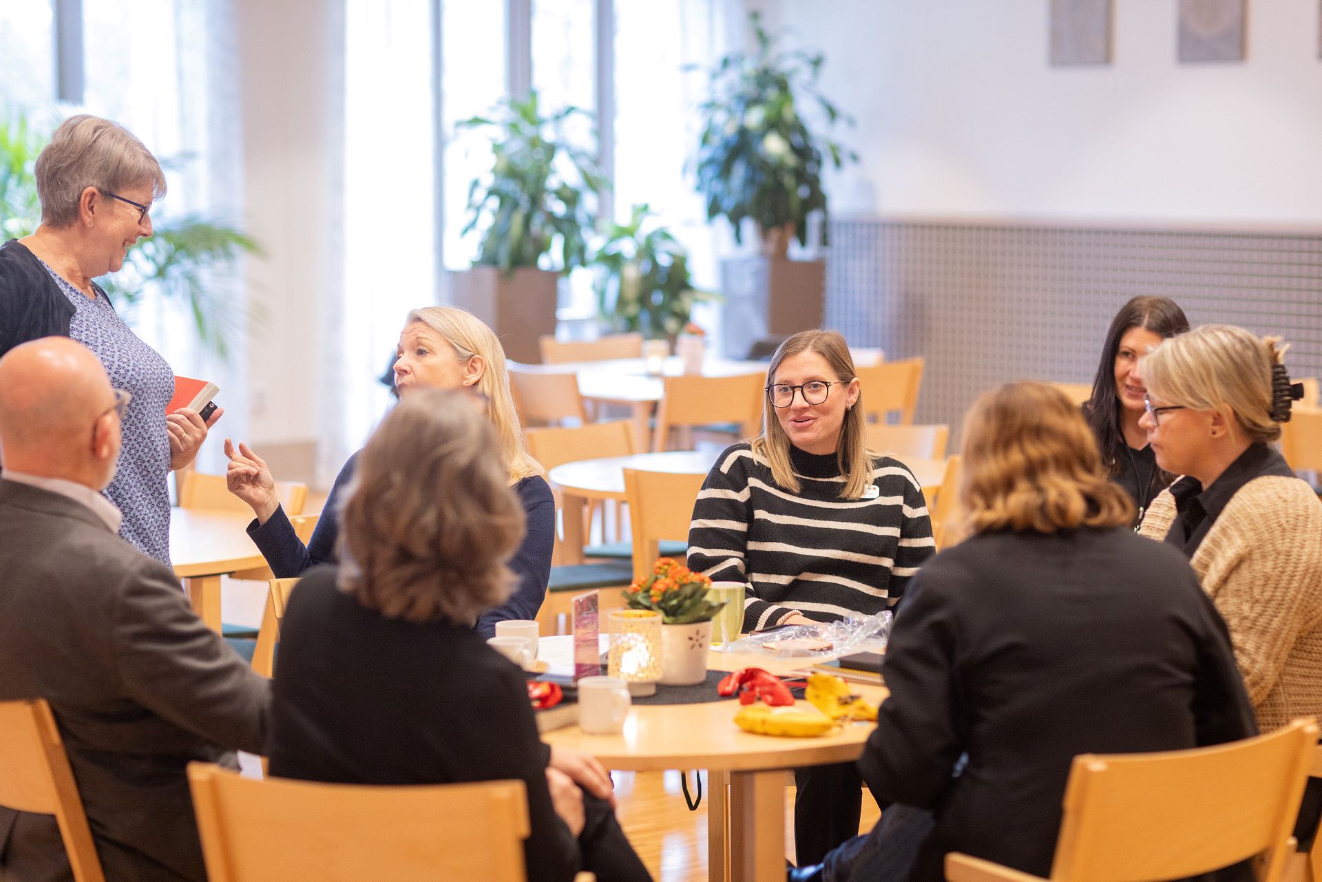 Flera vuxna personer sitter tillsammans vid ett runt bord och samtalar.