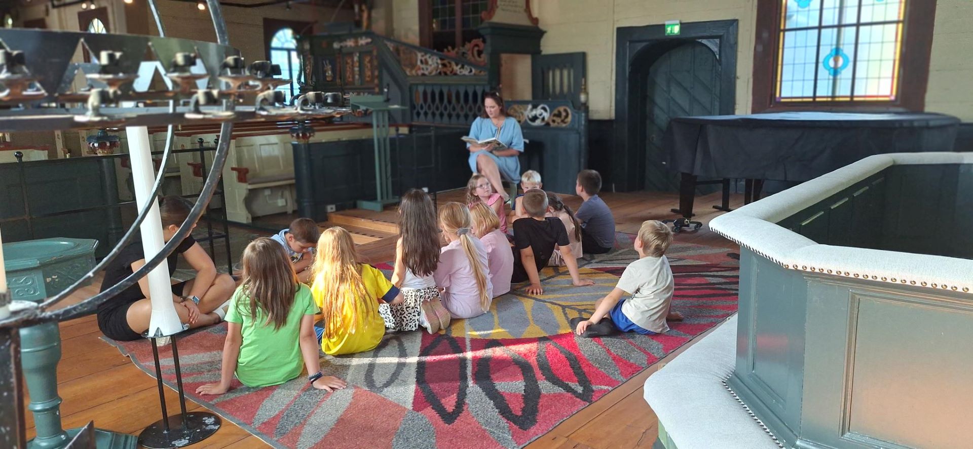 En barngrupp sitter på golvet och lyssnar på en berättelse om kyrkan