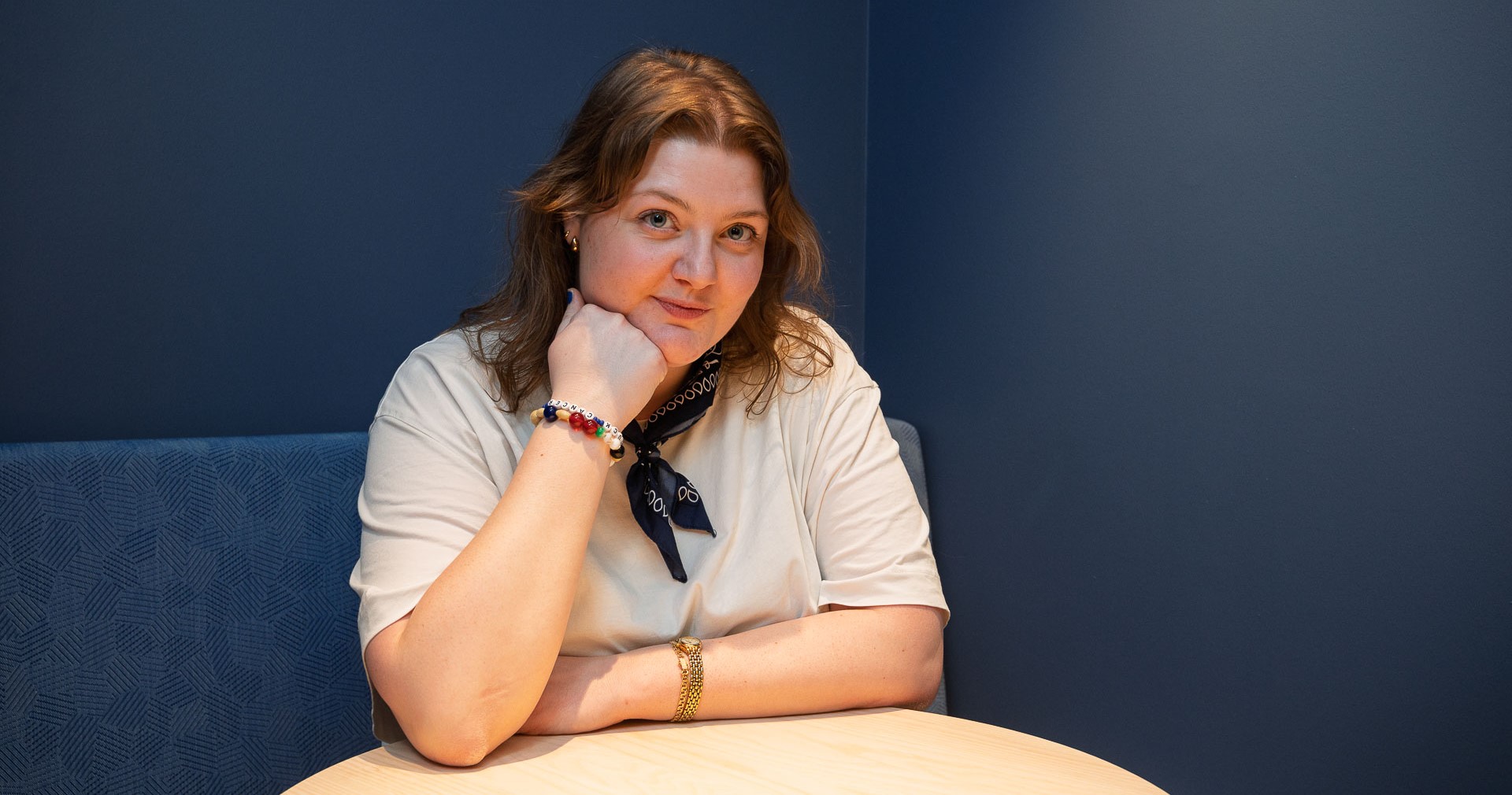 Alice lutar sig mot ett bord och lutar hakan på handen. 