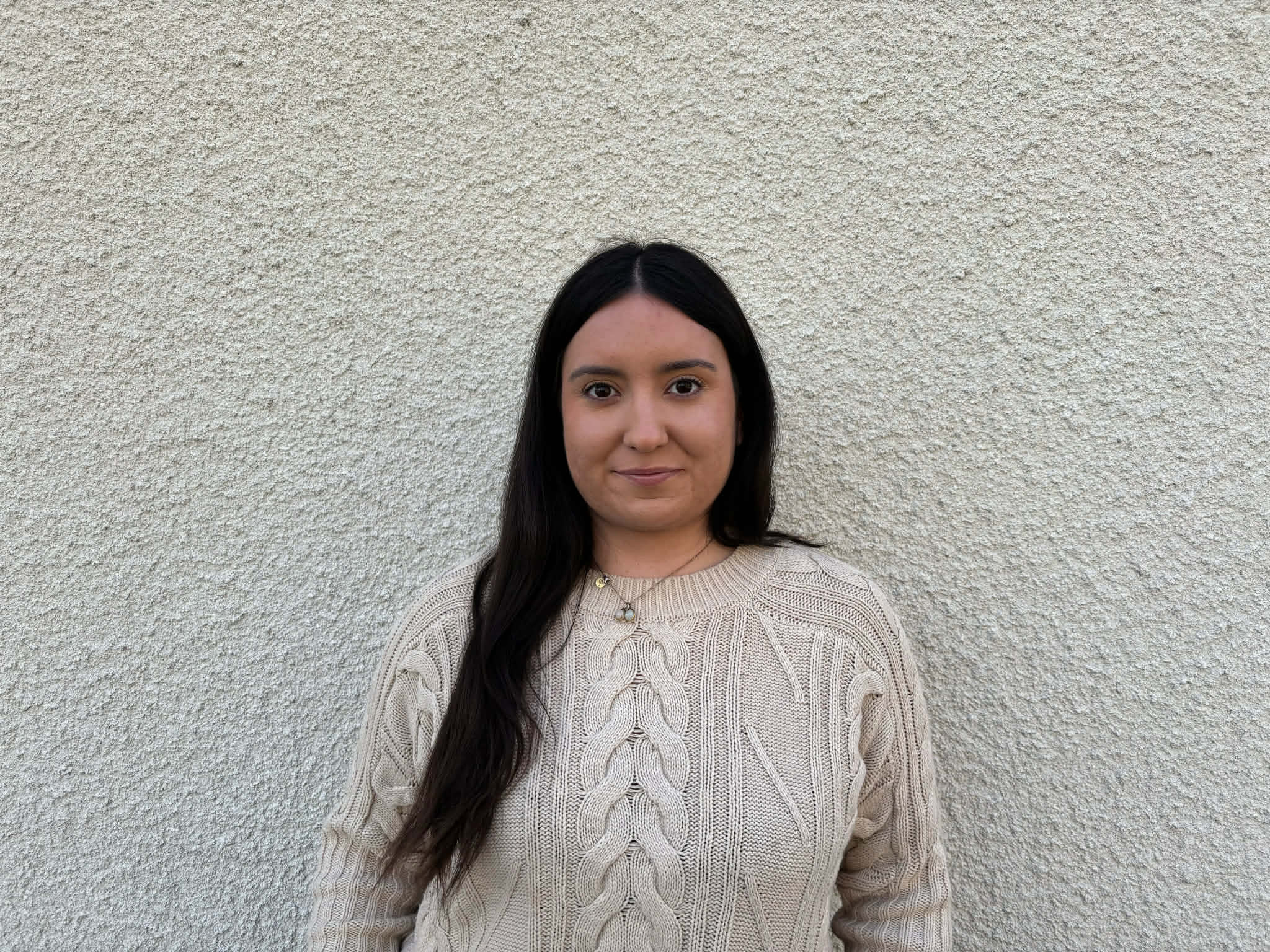 Olivia i halvfigur står mot en grå husfasad och ler lite in i kameran.