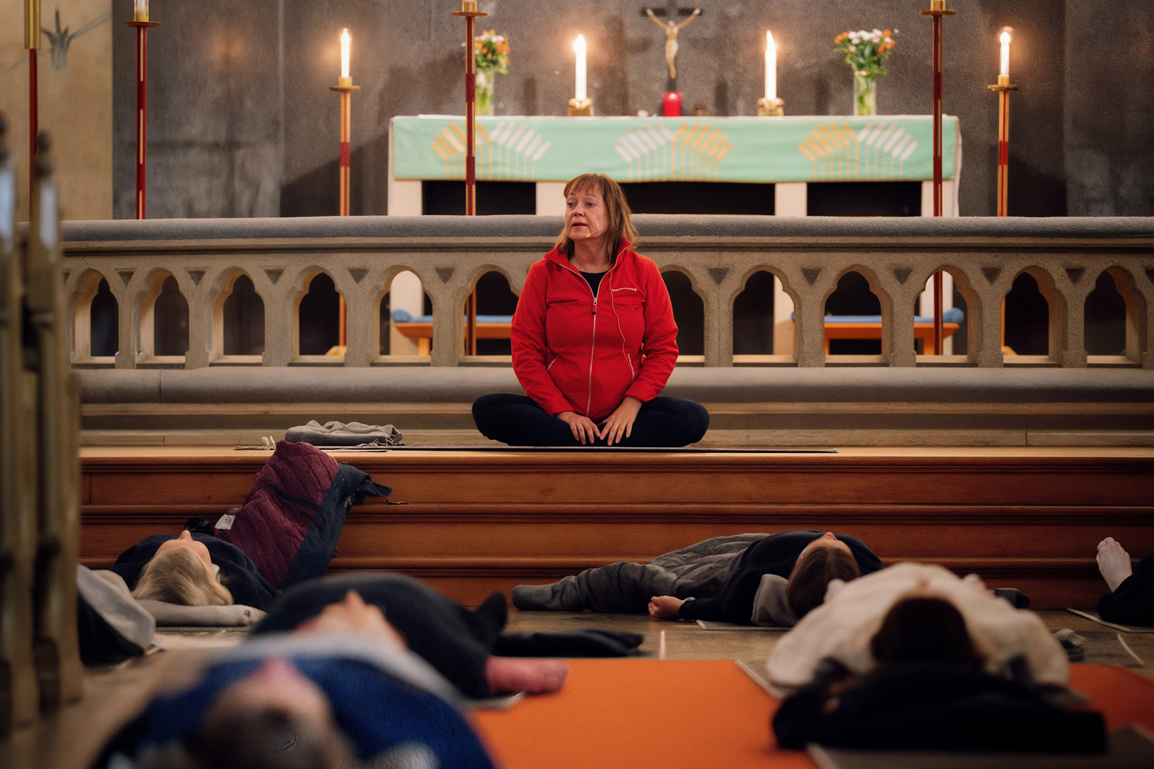 Maria leder medicinsk yoga i Oscarskyrkan. På altaret brinner levande ljus. Personer ligger i vila på yogamattor.