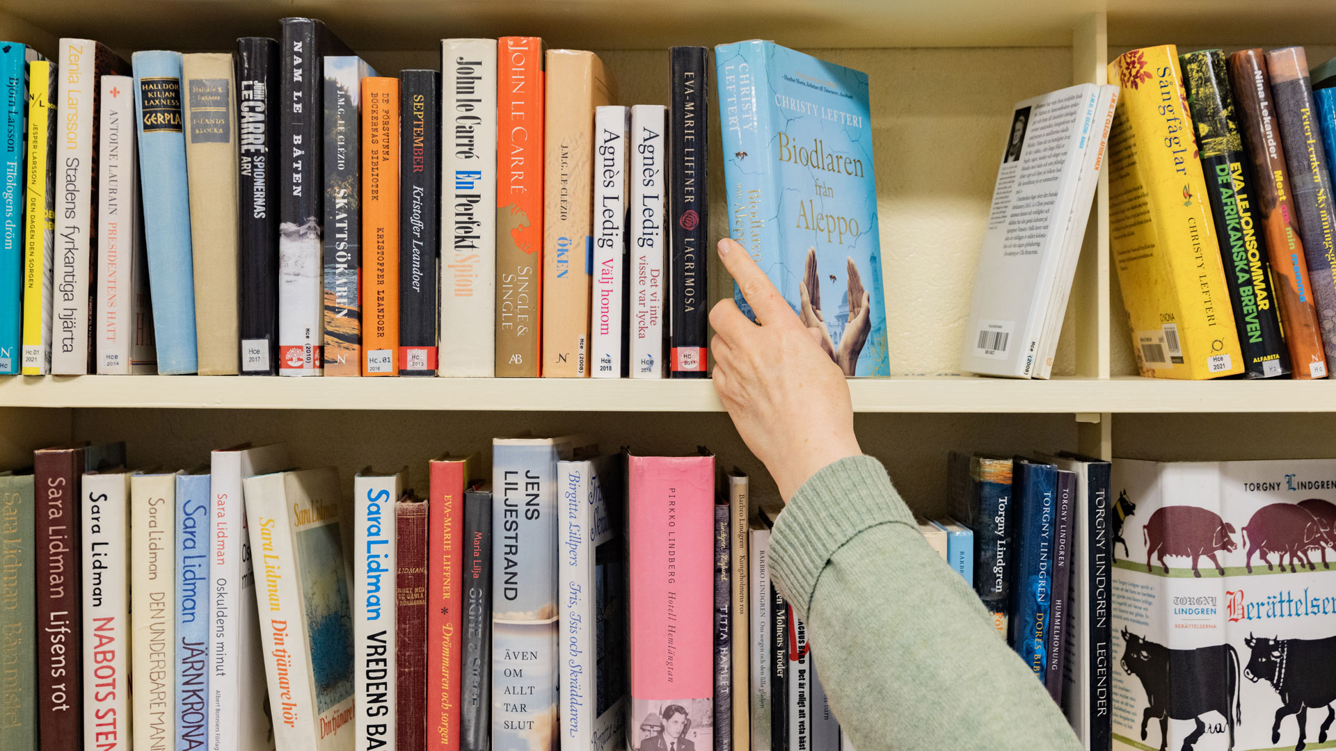 En hand sträcker sig efter en bok i en bokhylla full av böcker.