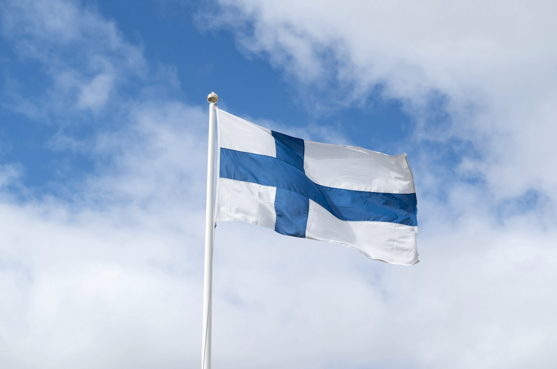En finsk flagga i blått och vitt mot en blå himmel med vita moln.