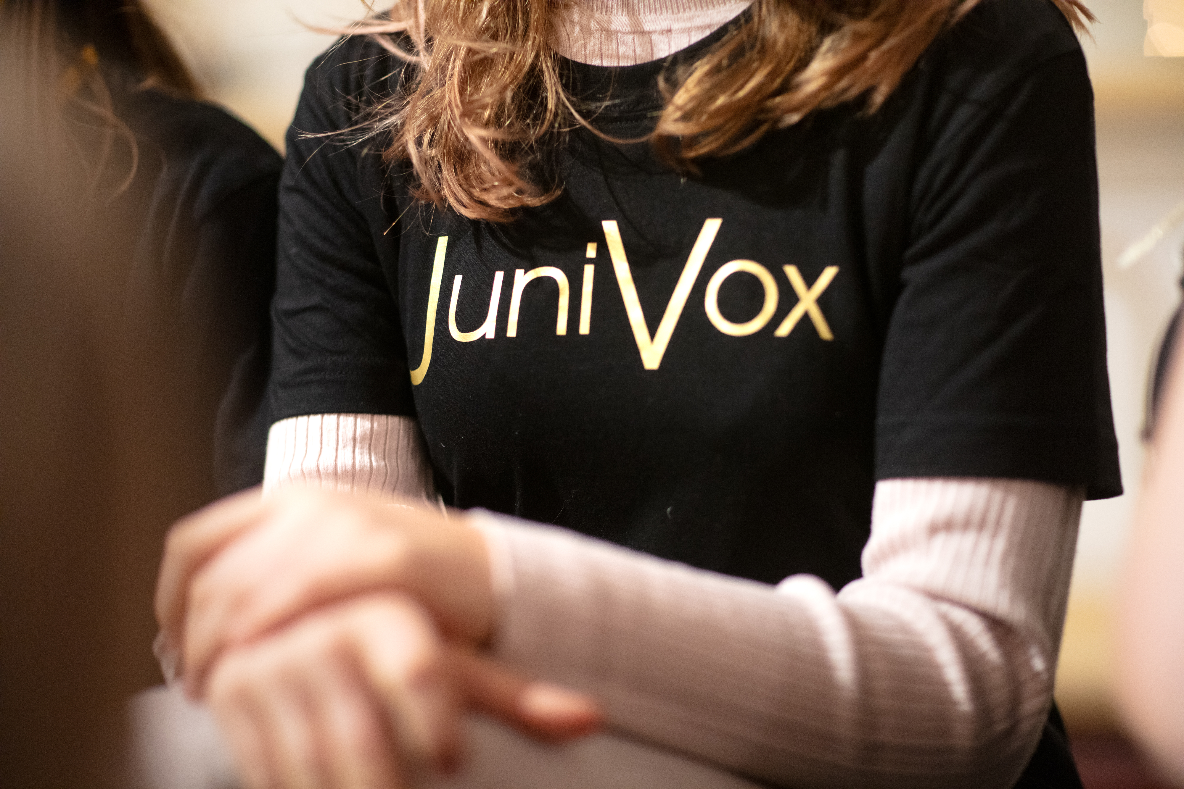 En tjej sitter med en t-shirt med tryck JuniVox på bröstet.