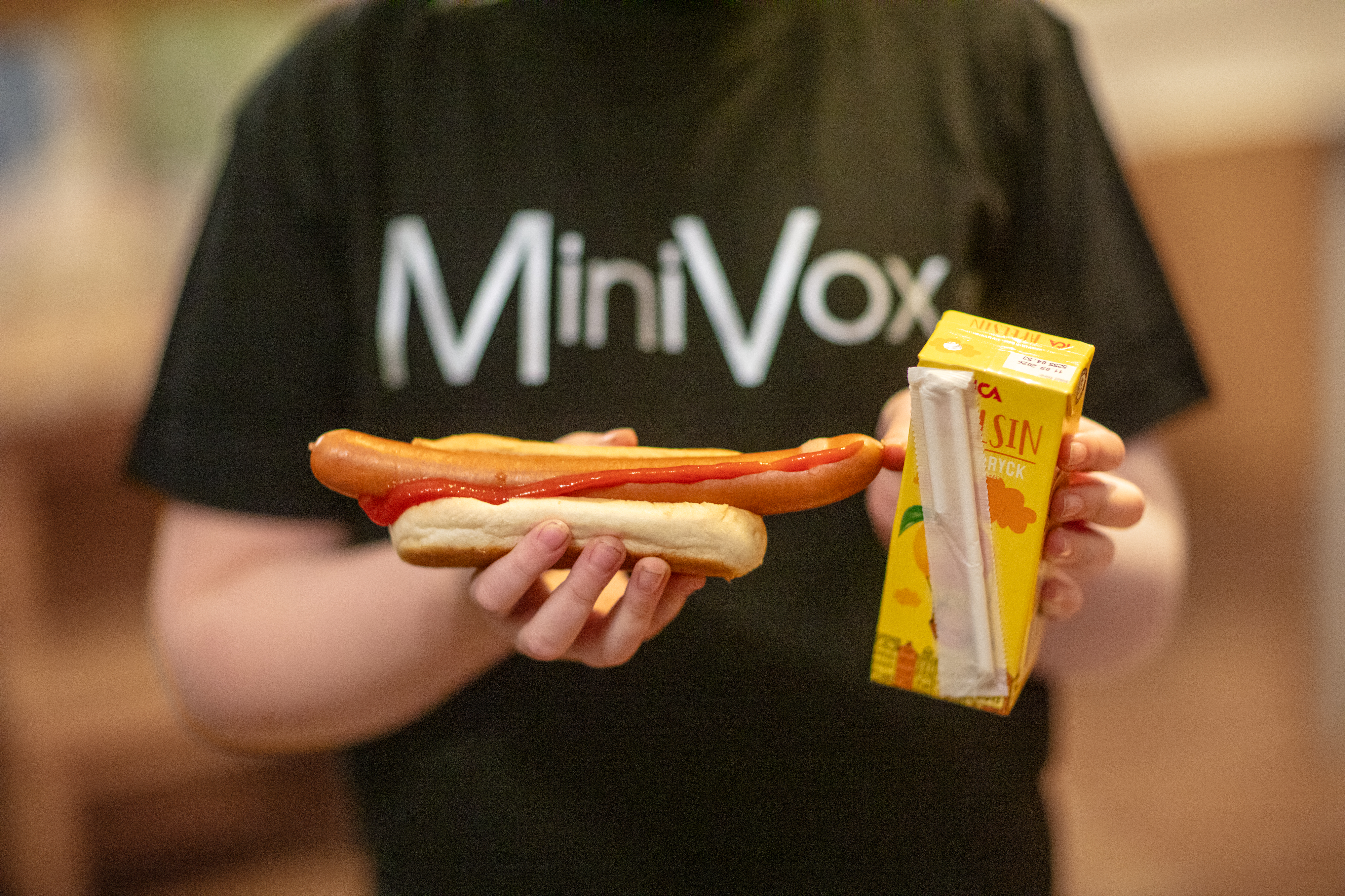 Ett barn i t-shirt med trycket MiniVox håller i en korv med bröd