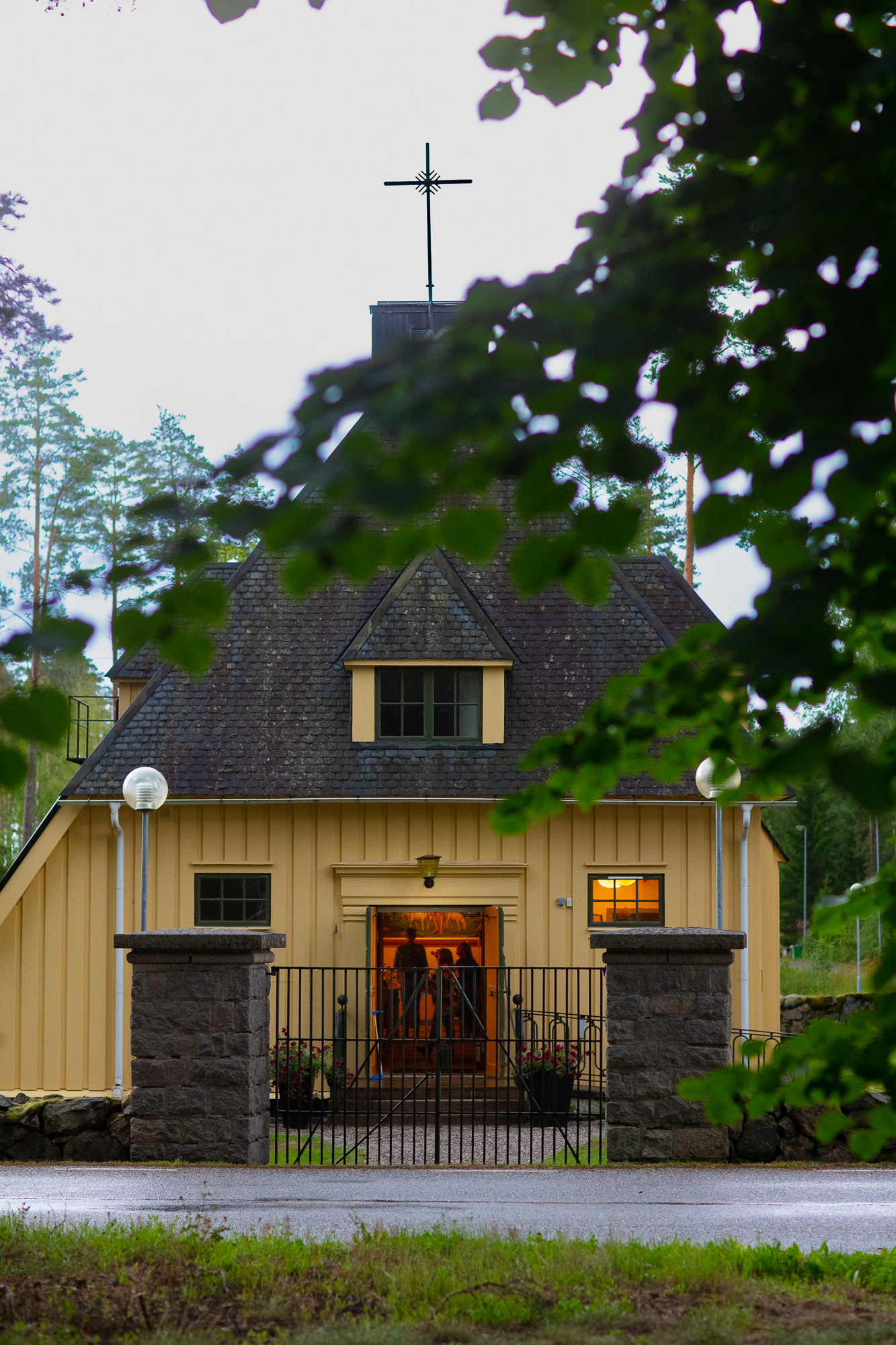 Spannarboda kyrka från kortsidan. Dörren är öppen och ljus syns där inne. Grönskande omgivning. 