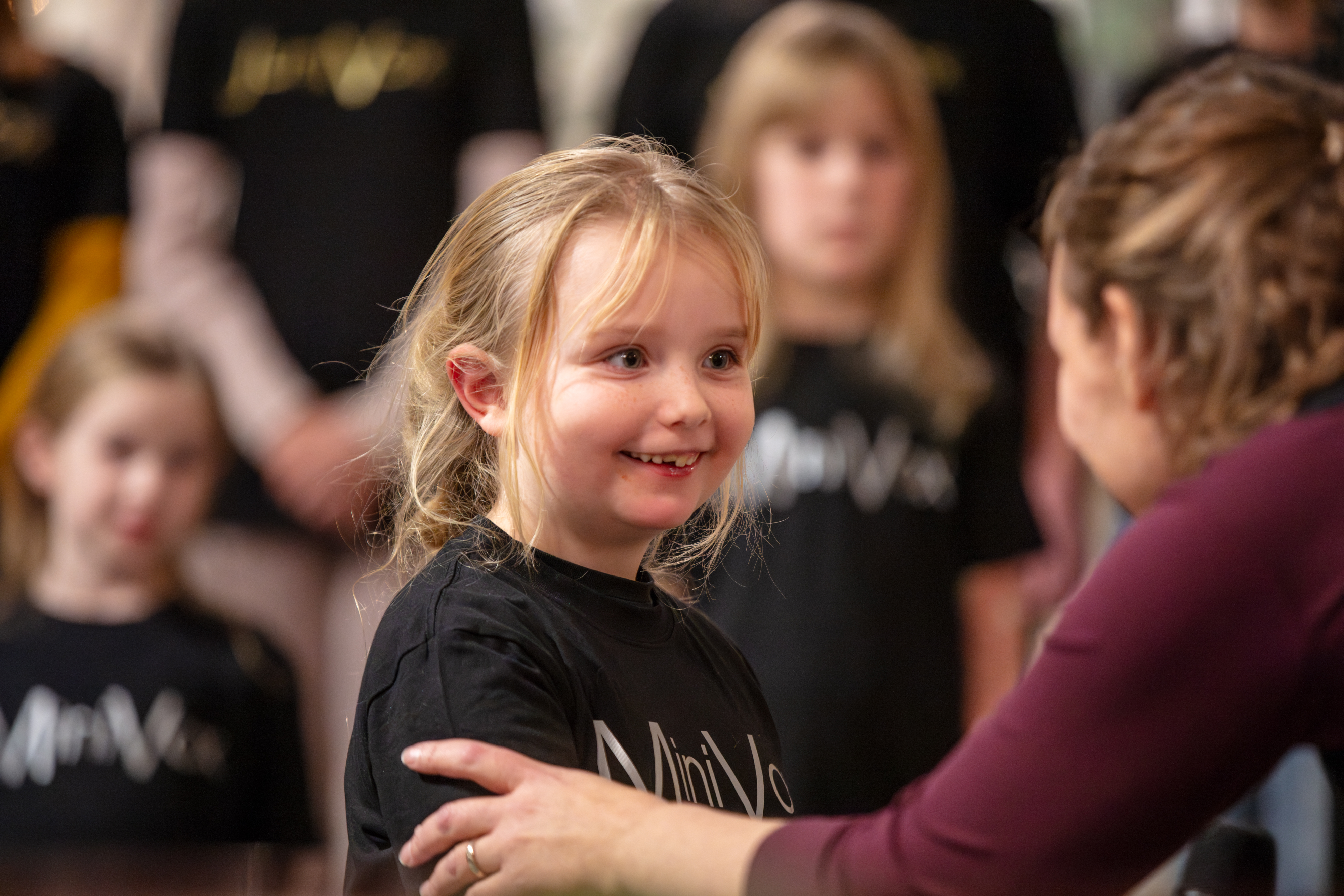 Ett barn tittar med glada glittrande ögon på sin körledare som lägger handen på barnets arm och berömmer för bra soloinsats. 