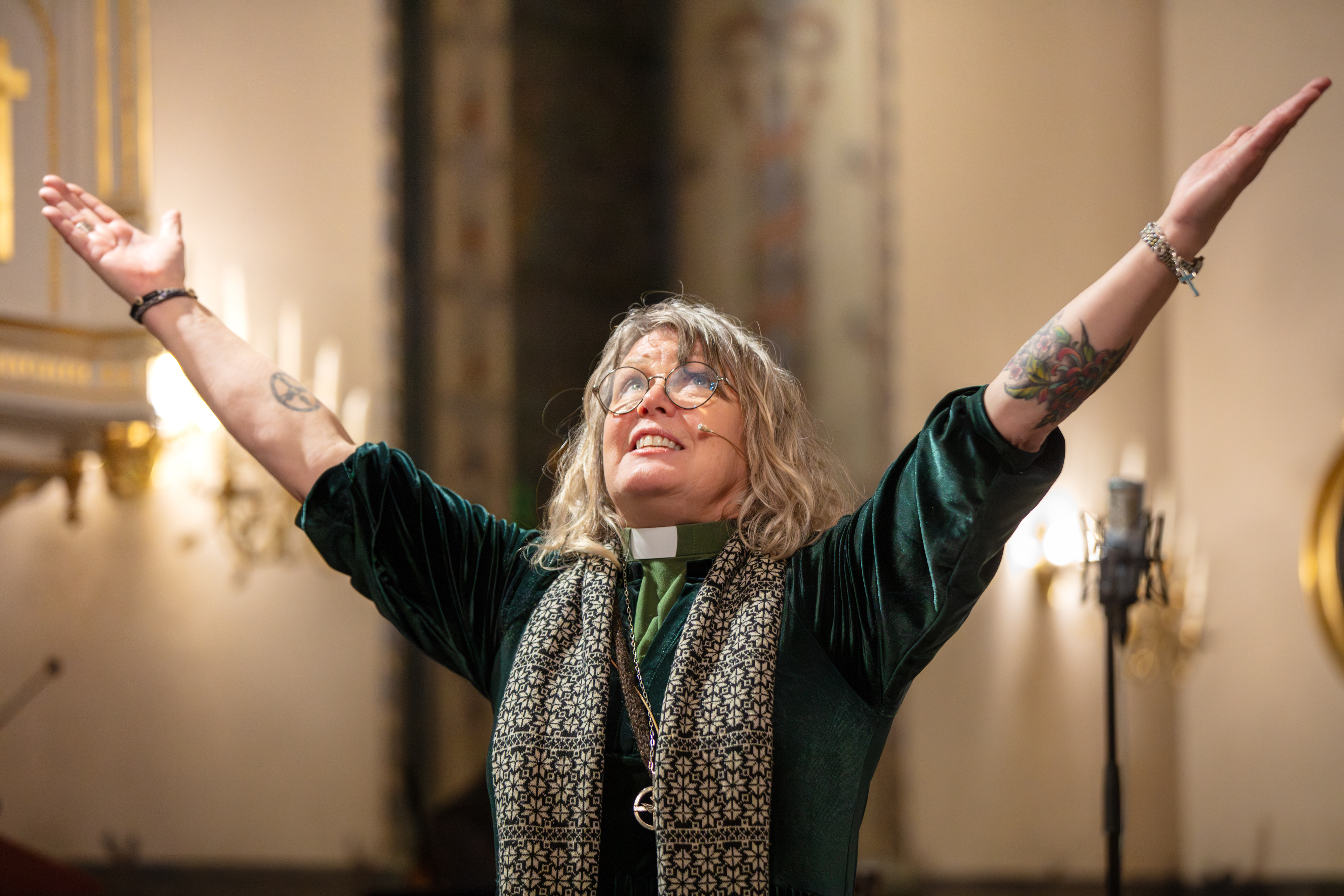 En dikaon sträcker upp sina händer i luften under en betraktelse i kyrkan och tittar längtansfullt uppåt.  