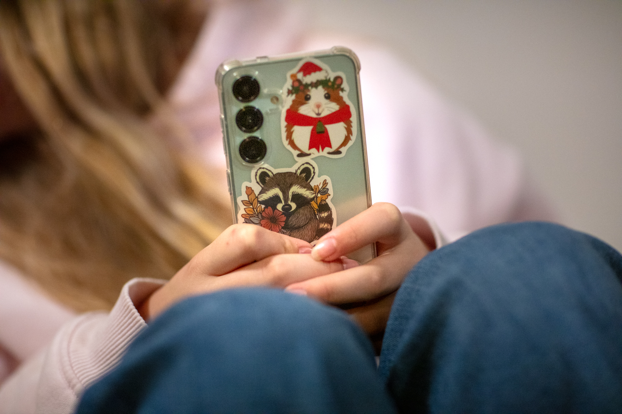 Ung person i rosa tröja sitter med sin mobil. Baksidan av mobilen syns och där sitter olika stickers. 