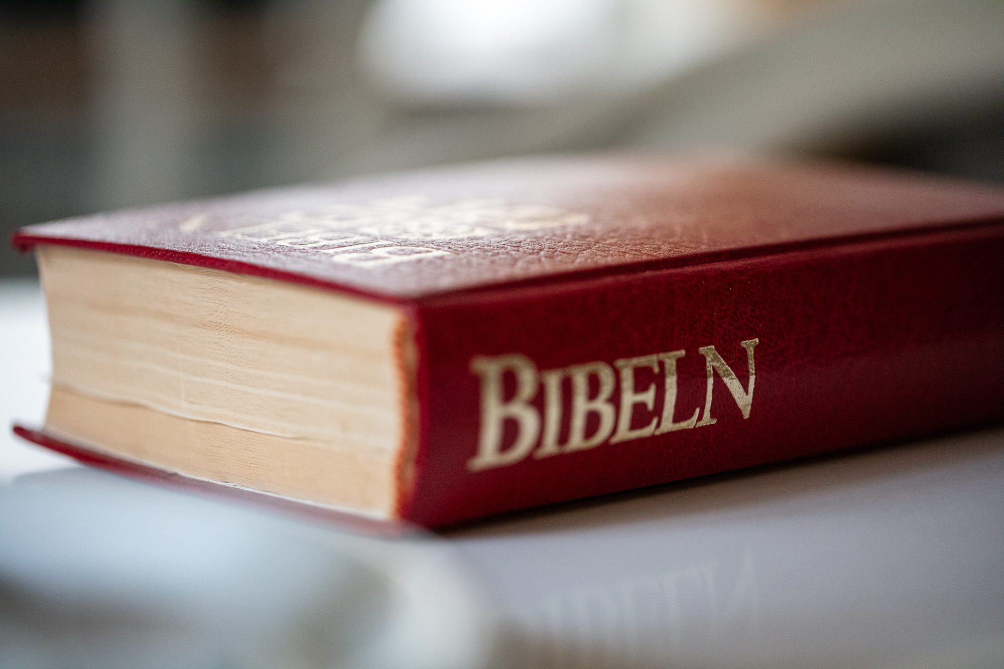En röd bibel med guldtext på ryggenl ligger på ett bord. 