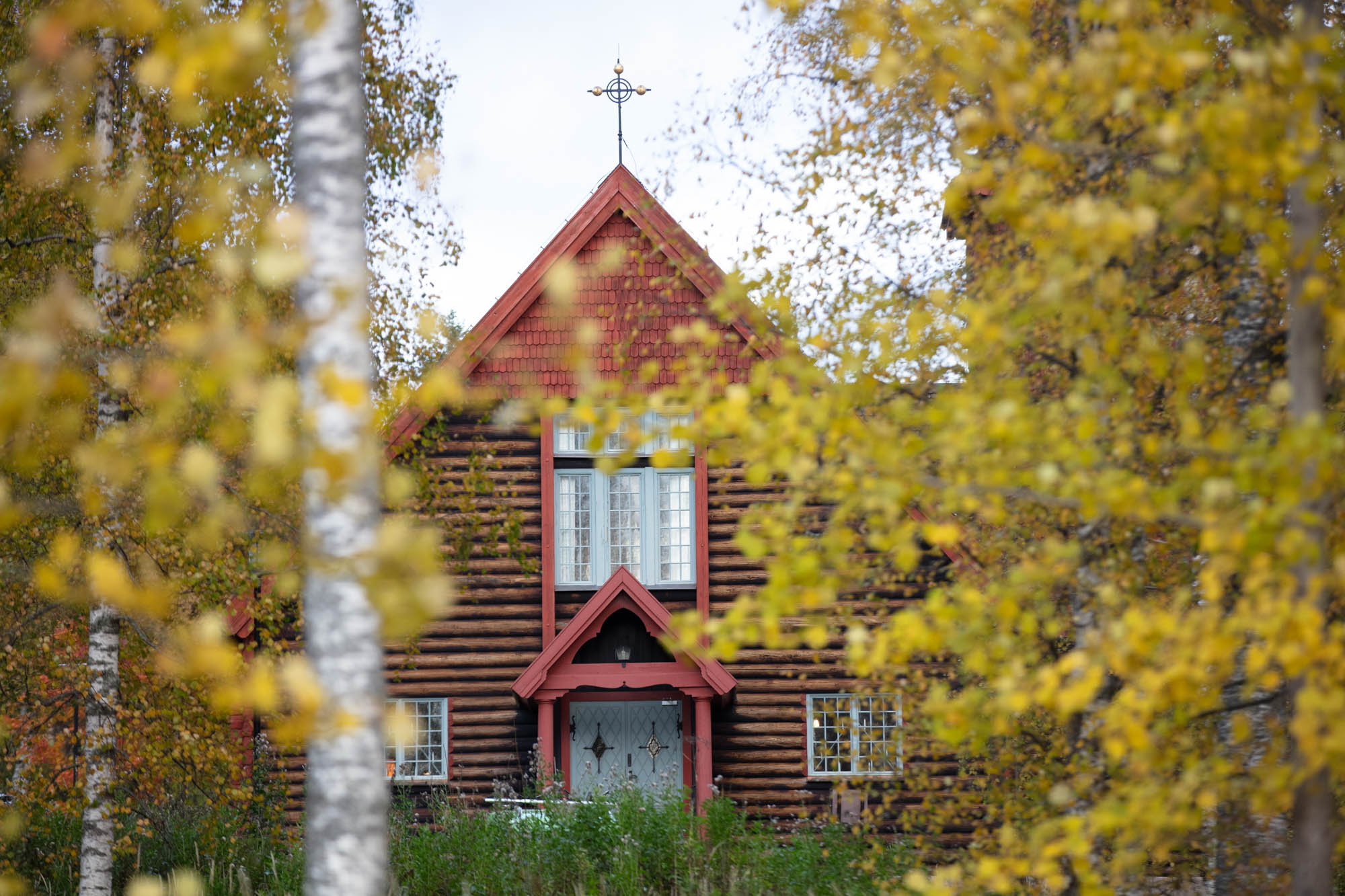 Du skymtar Hörkens kyrka genom lövtäckta grenar med höstfärgade löv