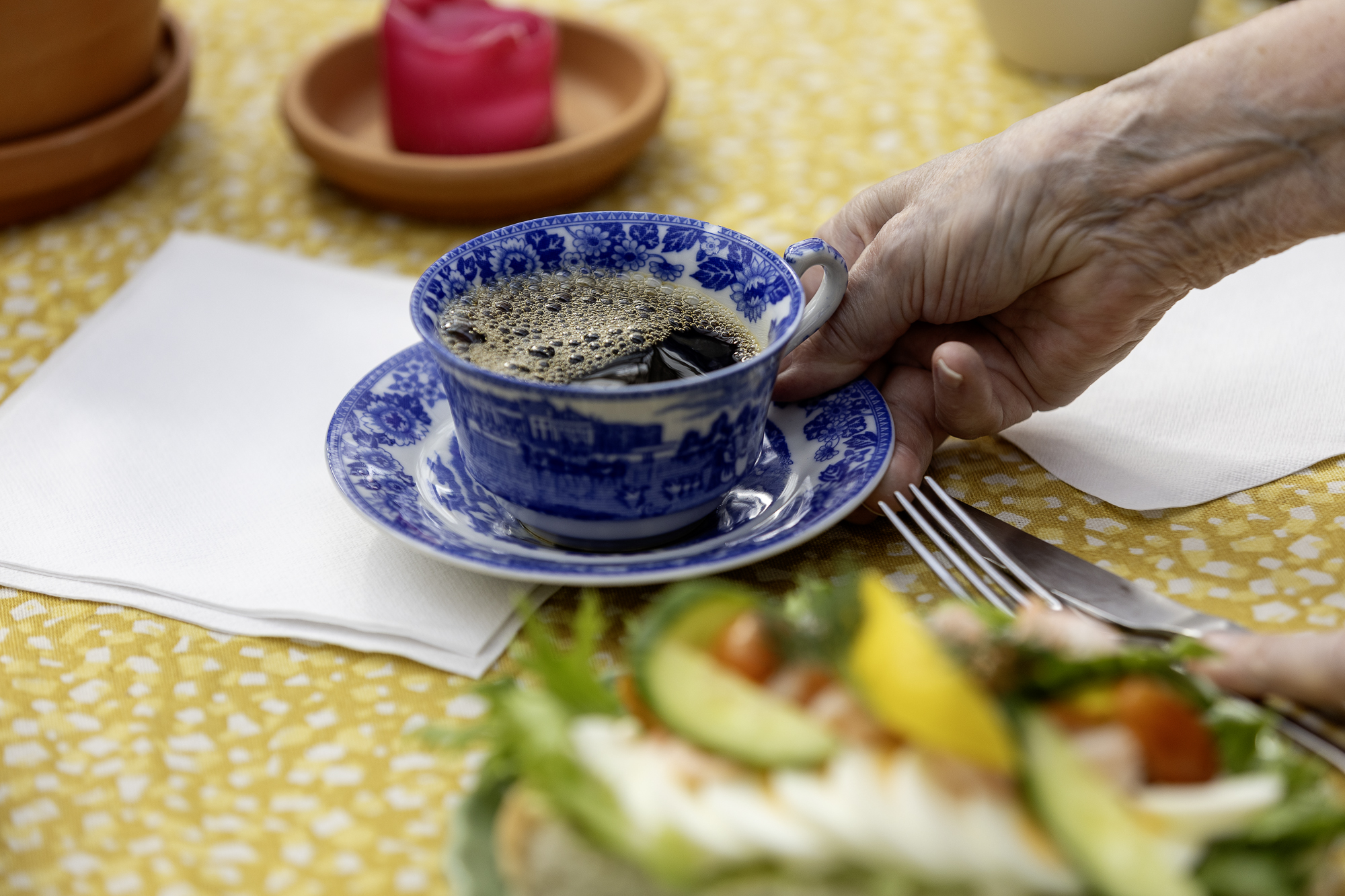 Blå porslinskopp med rykande kaffe ställs fram på ett bord