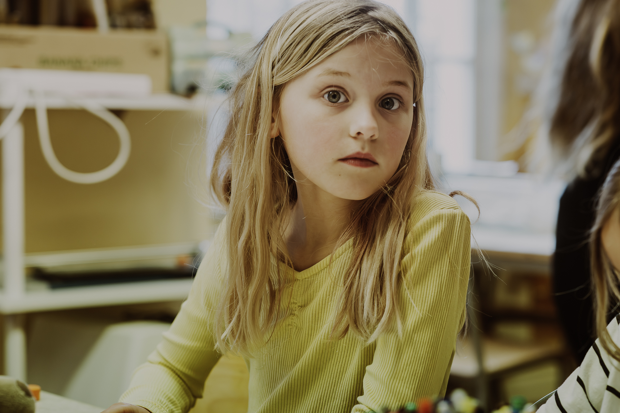 En tjej i gul tröja sitter i pysselrummet och titta in i kameran