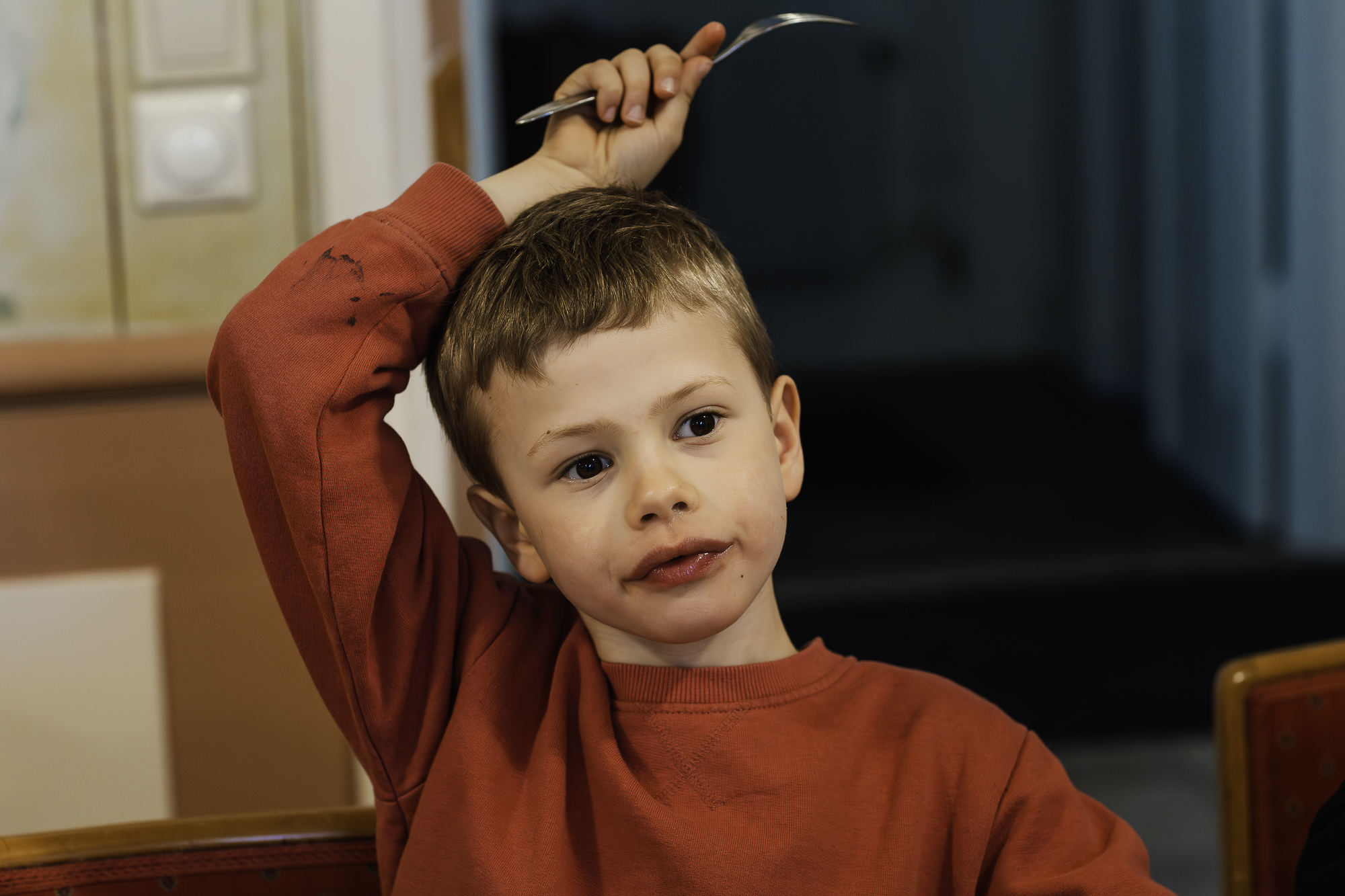 En pojke sitter och äter mellis med en gaffel i handen som han sträcker över sitt huvud