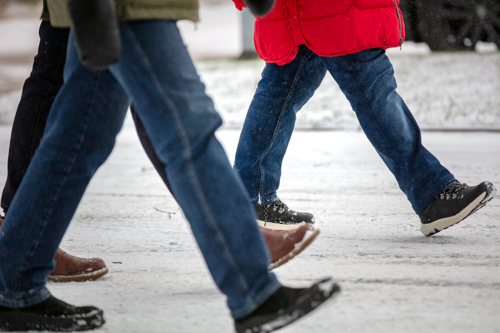 Du ser benen på flera personer som promenerar med raska steg framåt. 