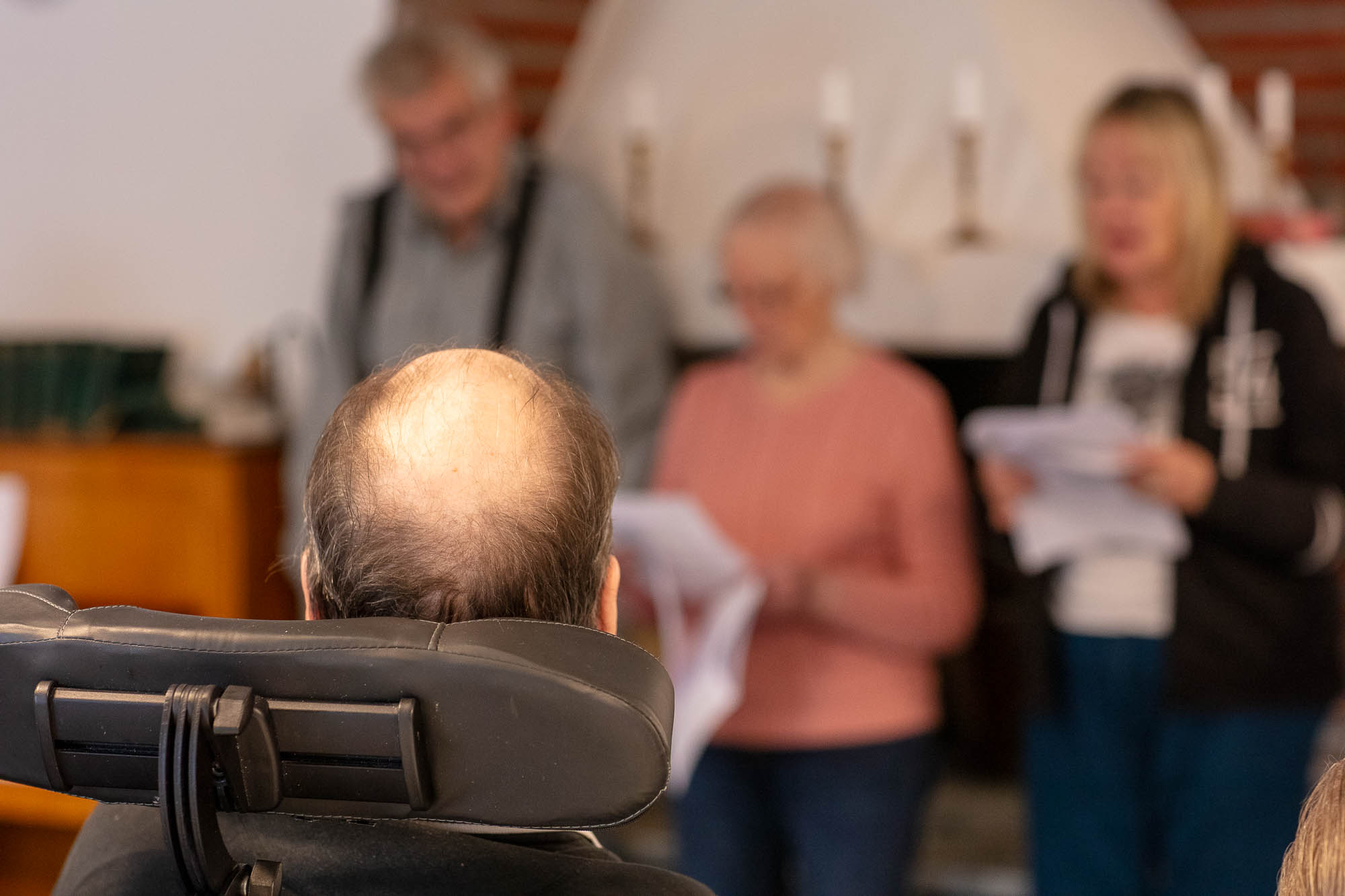 En äldre man sitter i rullstol och tittat på personer som sjunger