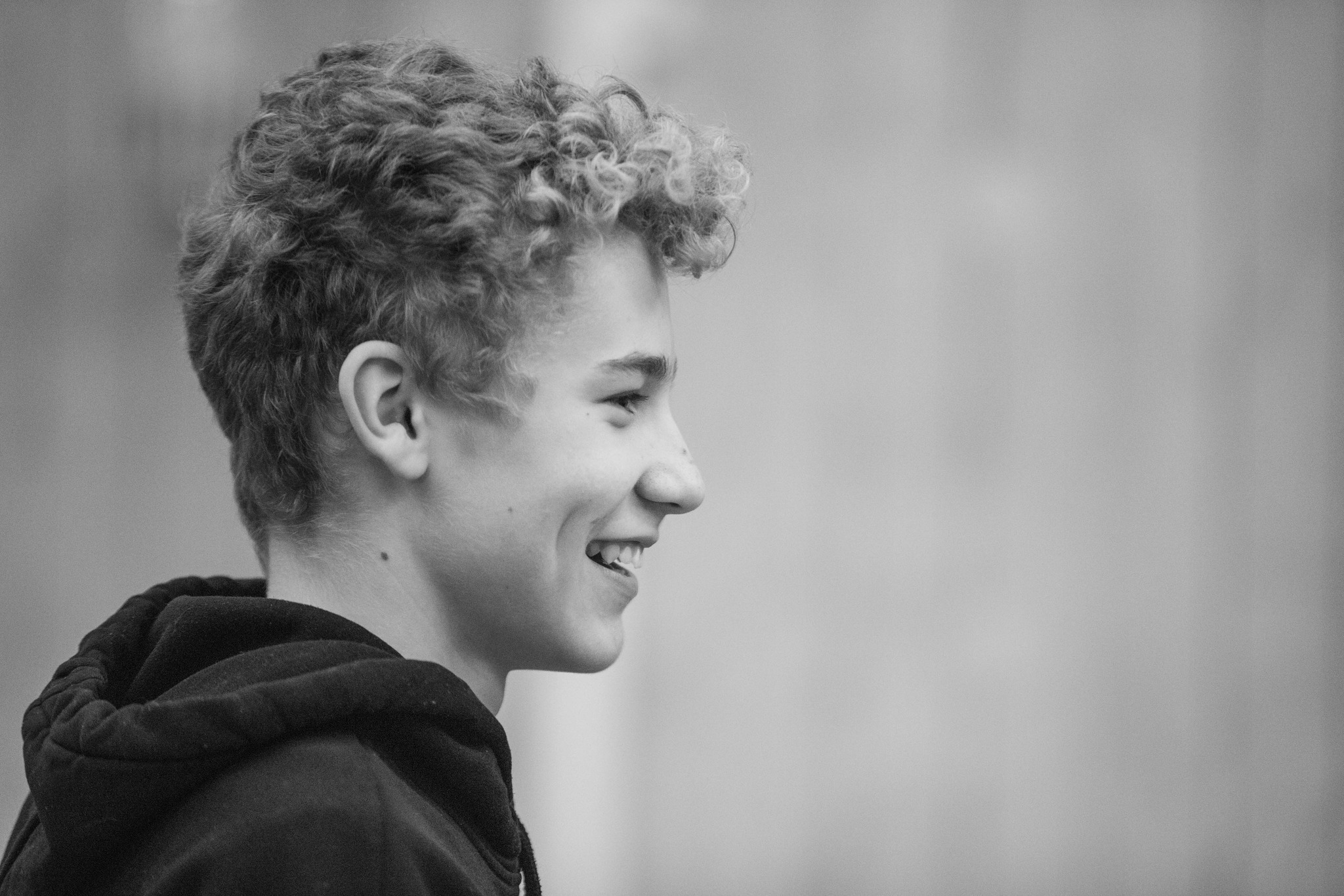 En glad ung pojke med lockigt hår och luvtröja.