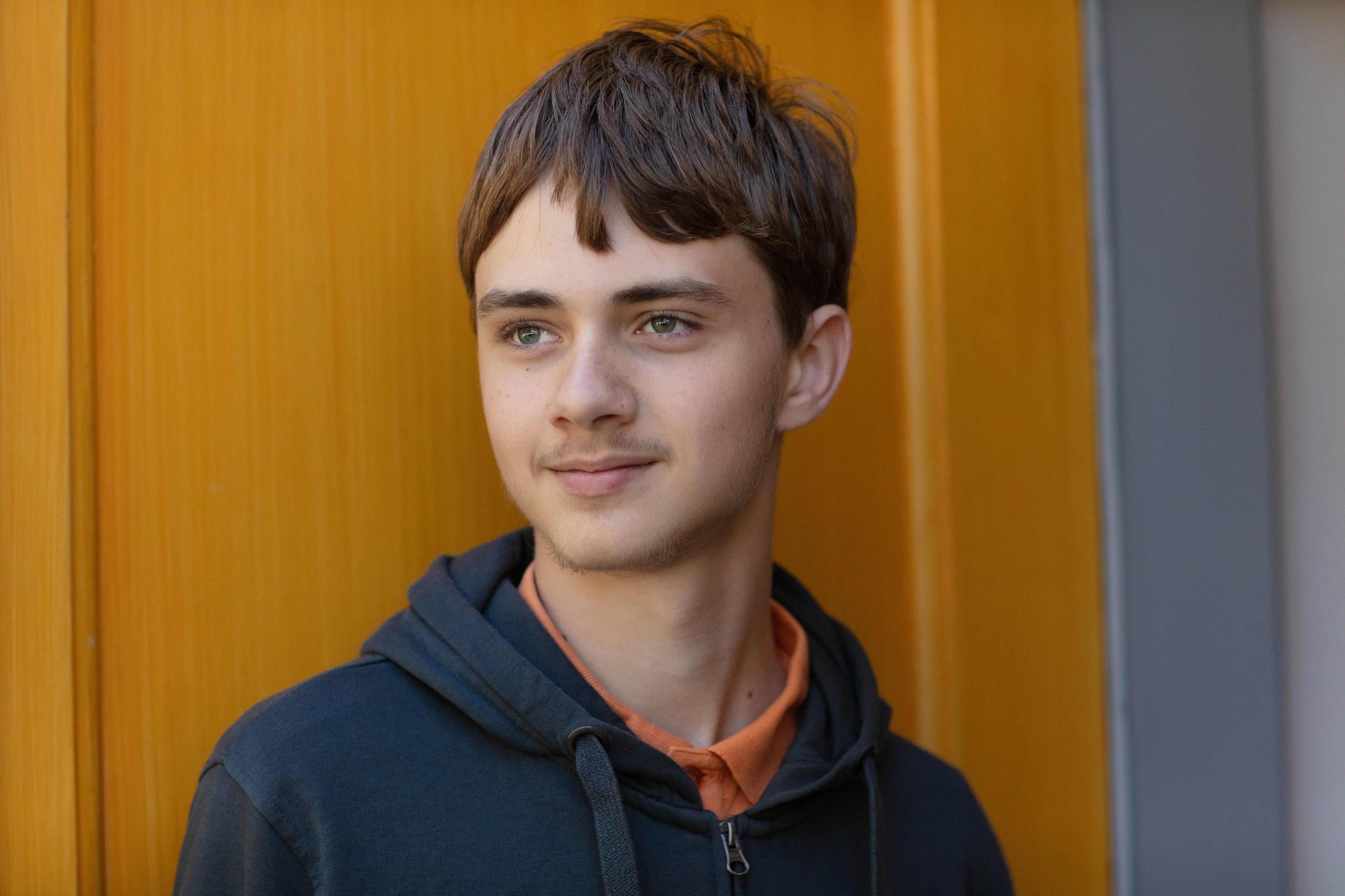 Porträtt på en ung kille i mörkt hår ståendes mot en gul kyrkport. 