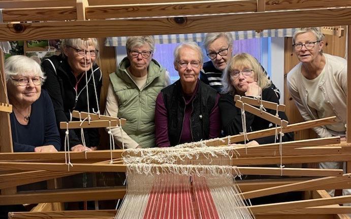 Inifrån vävstugan med deltagare som tittar genom en vävstol.