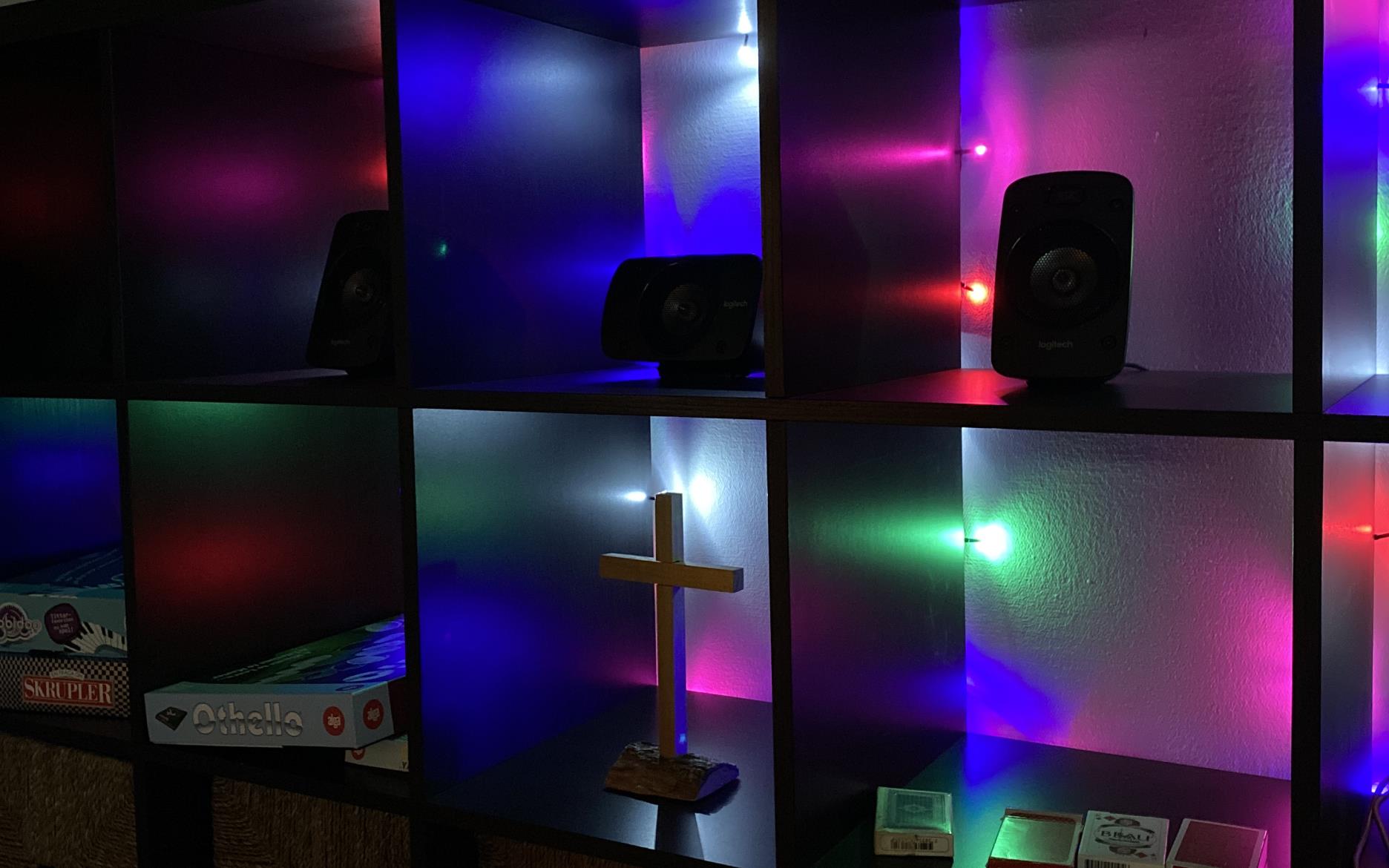 Ett kors i en svart bokhylla full med neonljus i blått, grönt och rosa.