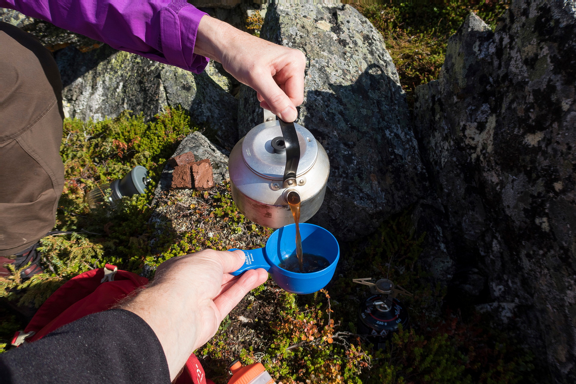 En hand håller en kaffekanna och häller upp i en annans mugg