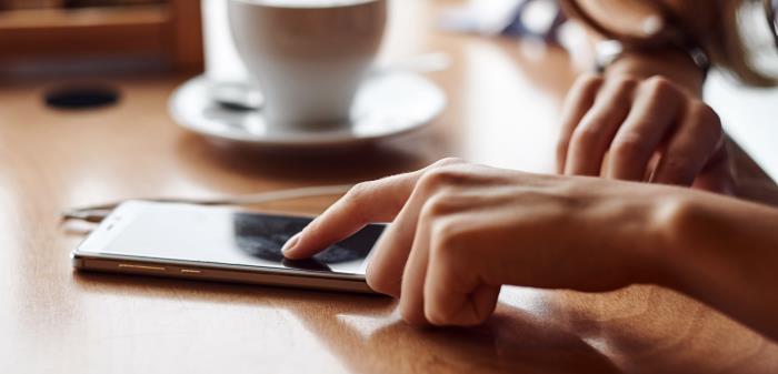 En person med en kopp kaffe som använder sin smartphone.