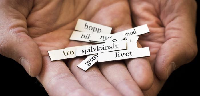 Närbild på två händer som håller i några kylskåpsmagneter med ord. Orden som syns är hopp, tro, självkänsla, livet och mod.