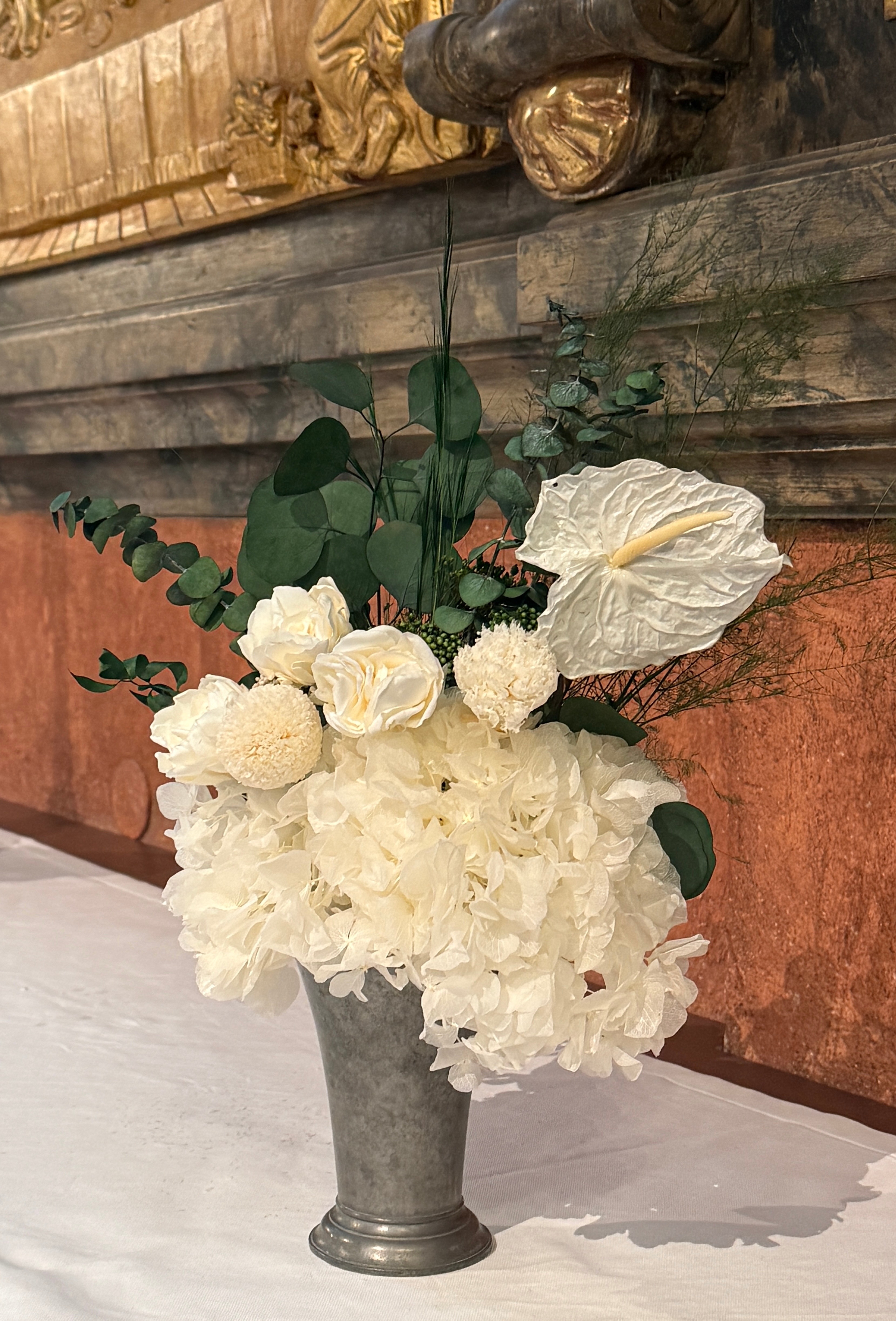 Vita konserverade blommor står i en vas på ett altare