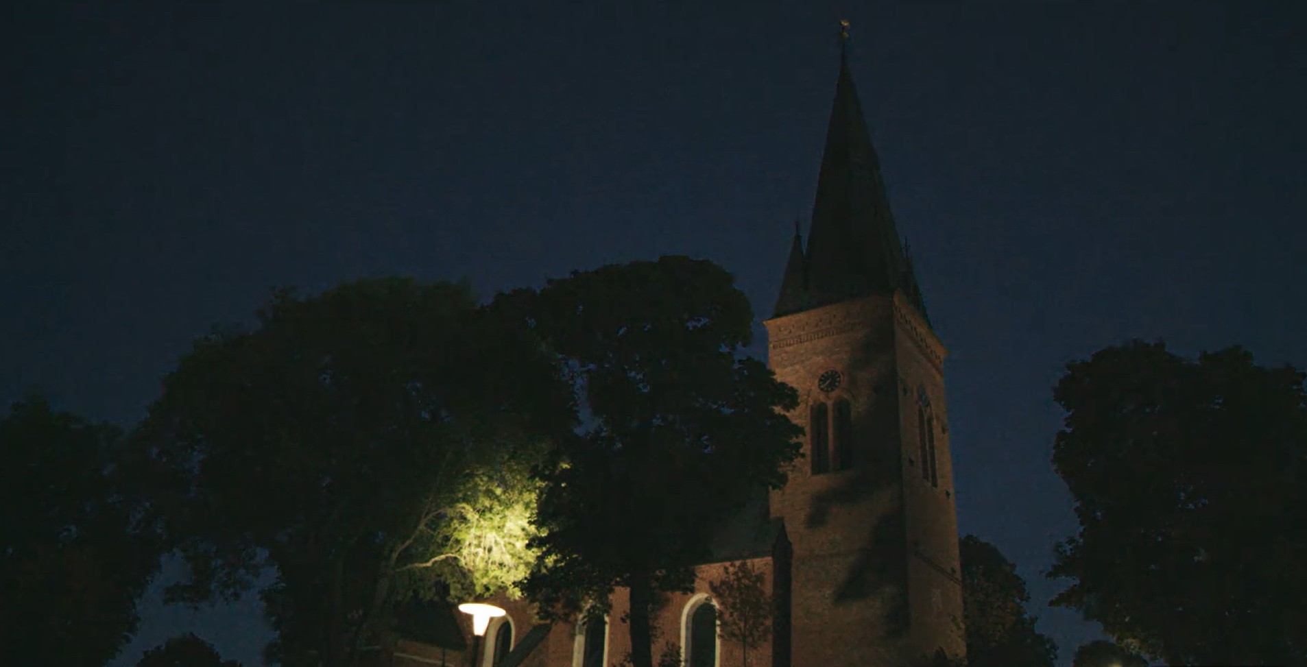 Bilden visar en typisk kyrka i skymning. En ljuspunkt kommer från en lykta i förgrunden.