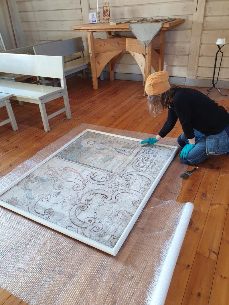 En person arbetar på golvet med renovering av en gammal väggmålning