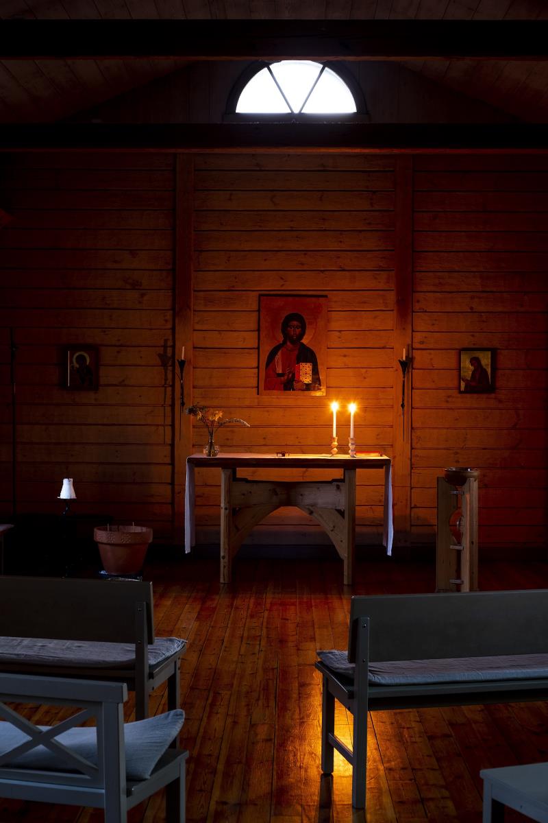 Altare i trä med två tända ljus ovanpå och en ikon på väggen bakom