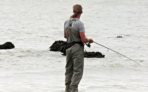 En person som står i vattnet och fiskar med fiskespö 