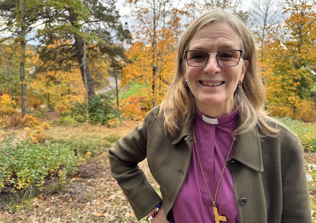 Biskop Marika framför träd i höstfärger vid promenad på Vårdnäs stiftsgård