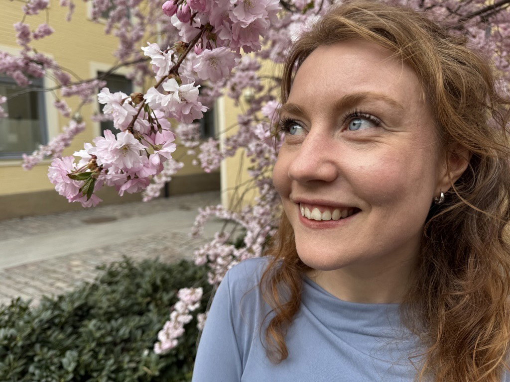 Prästkandidat Maria Blank tittar upp mot himlen med ett vackert blommande träd i bakgrunden.