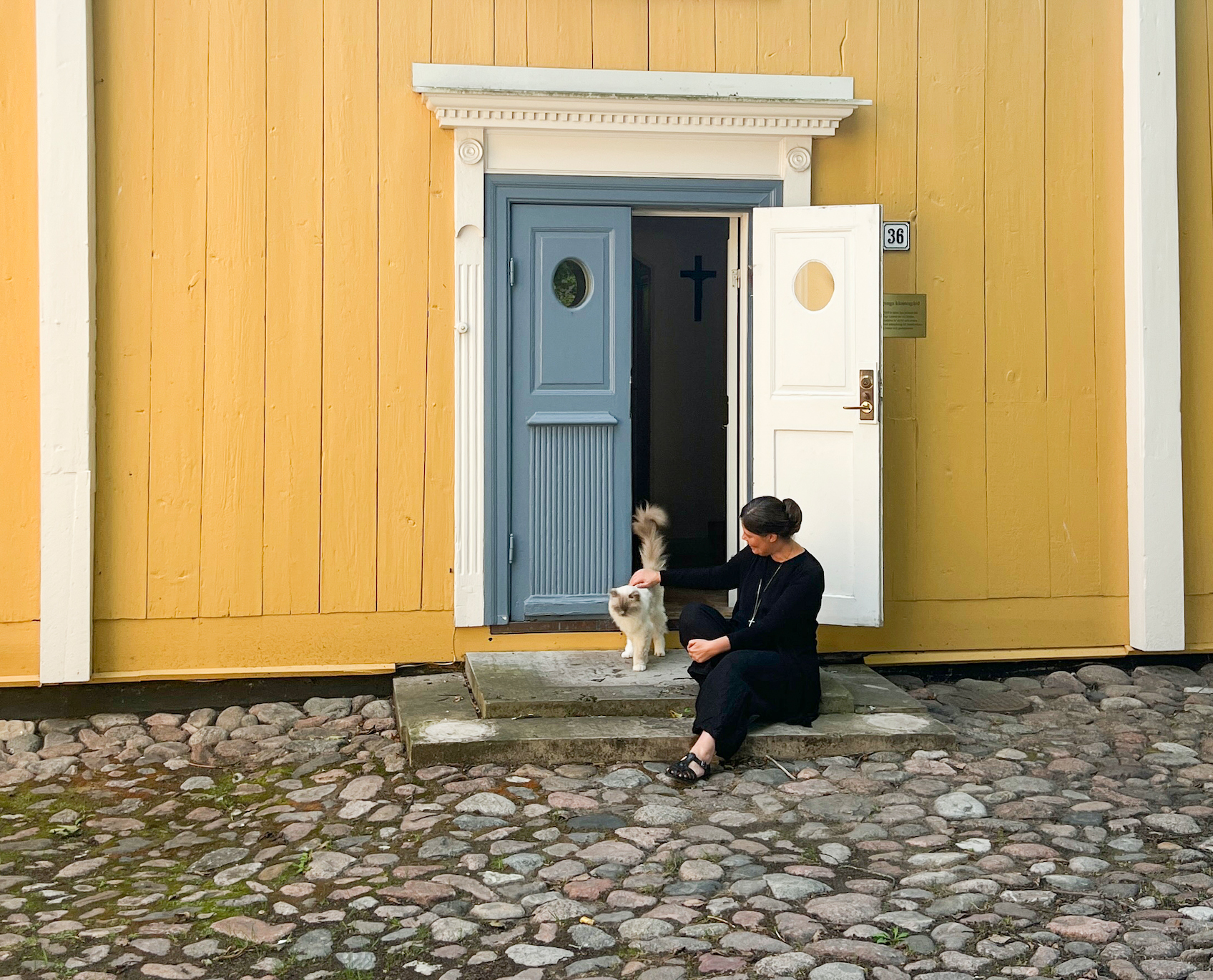 Syster Therése tillsammans med katten Albert vid Linköpings klosters gula husvägg