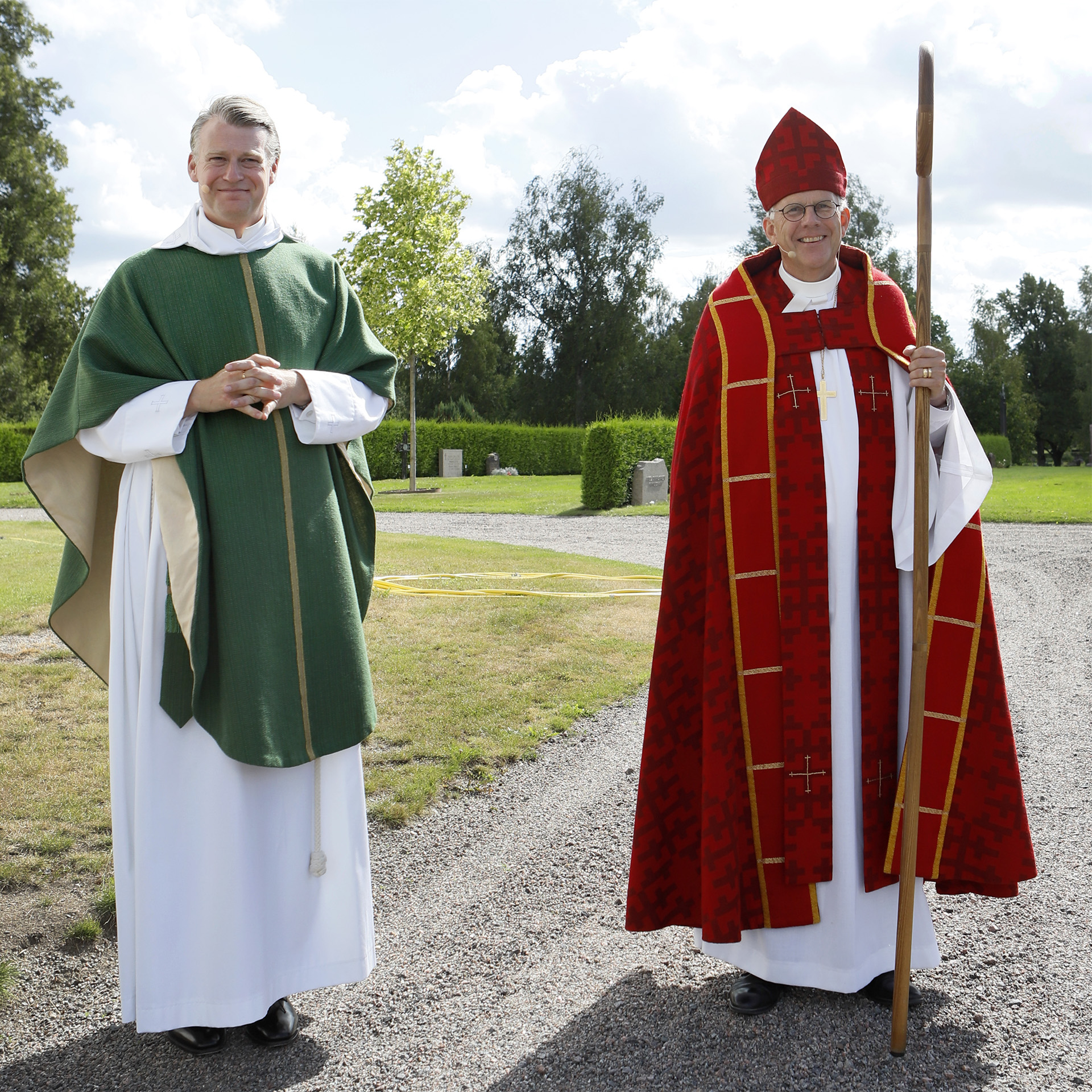 Kyrkoherde Pär Österlund och biskop Martin Modéus står på kyrkogården en fin sommardag, båda klädda i ceremoni-dräkter inför mottagningsmässan.